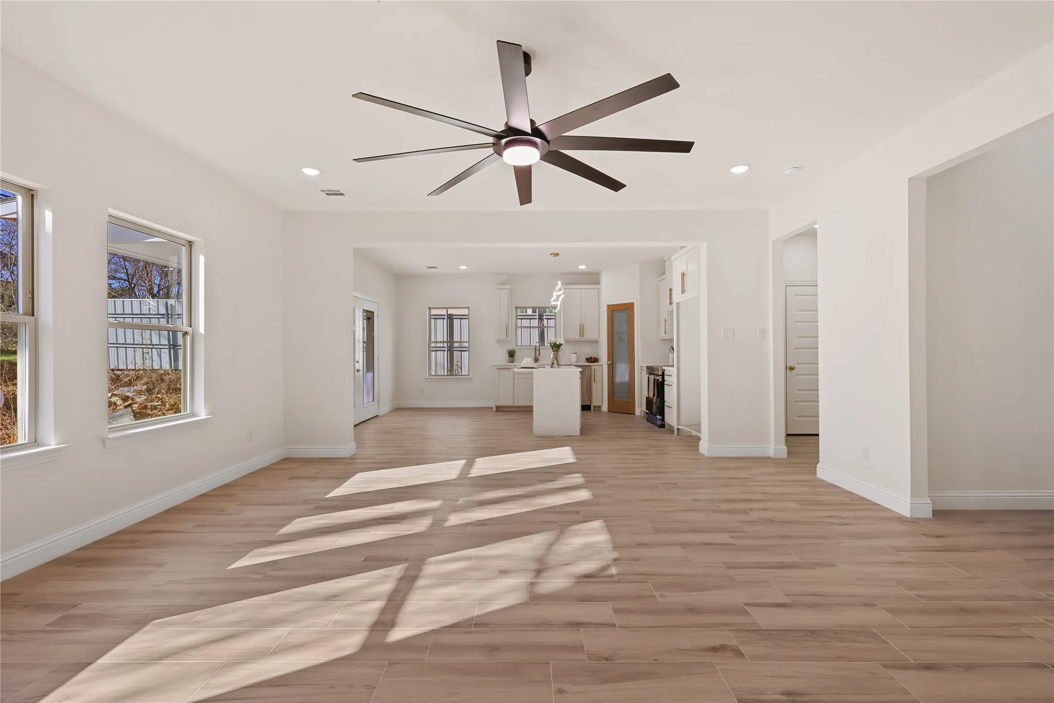Spacious room featuring wood-finish flooring, recessed lighting, a modern ceiling fan, and multiple windows
