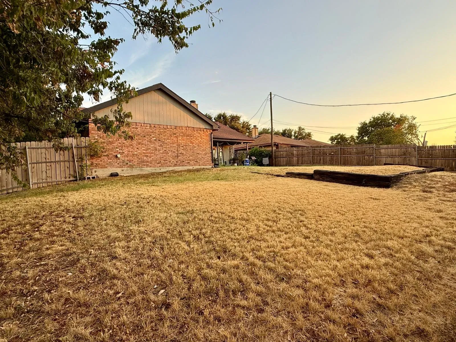 Expansive rear yard with privacy fencing, brick exterior, and a defined raised garden bed