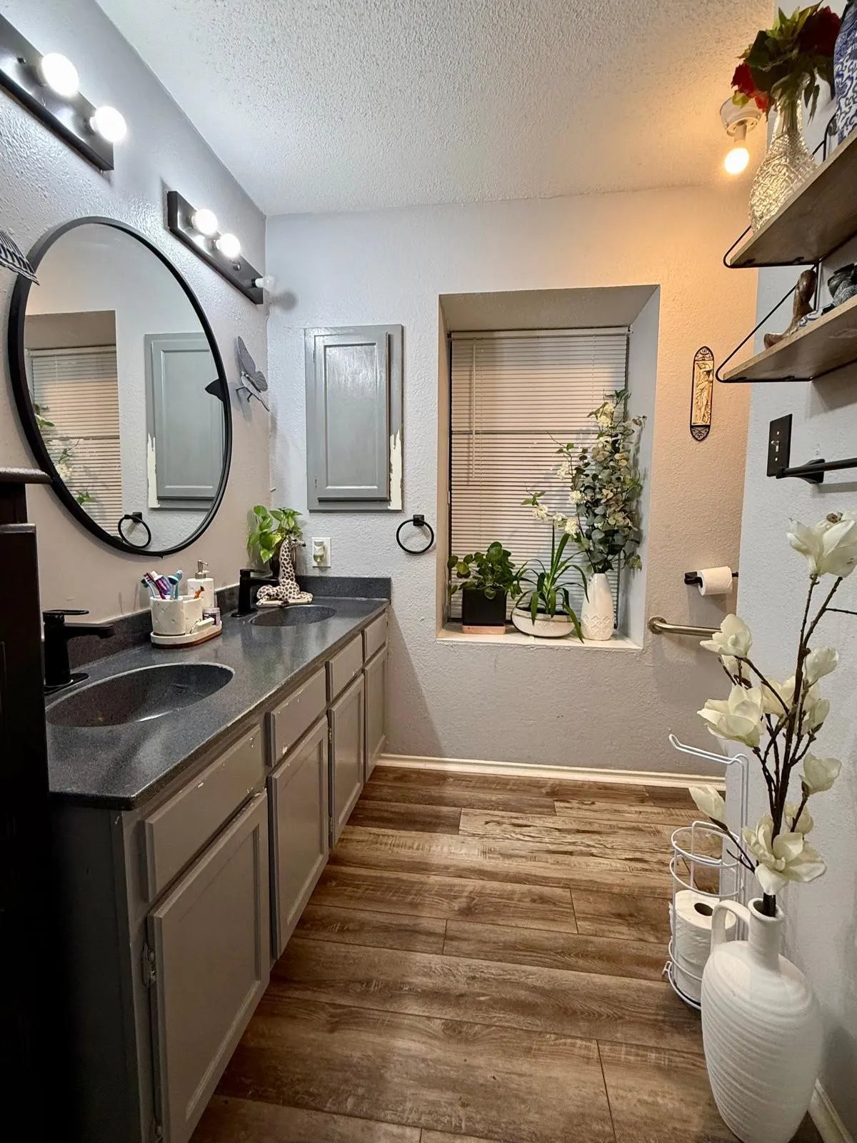 Double vanity with integrated sinks, wood-finish flooring, built-in recessed window shelving, and wall-mounted storage shelves