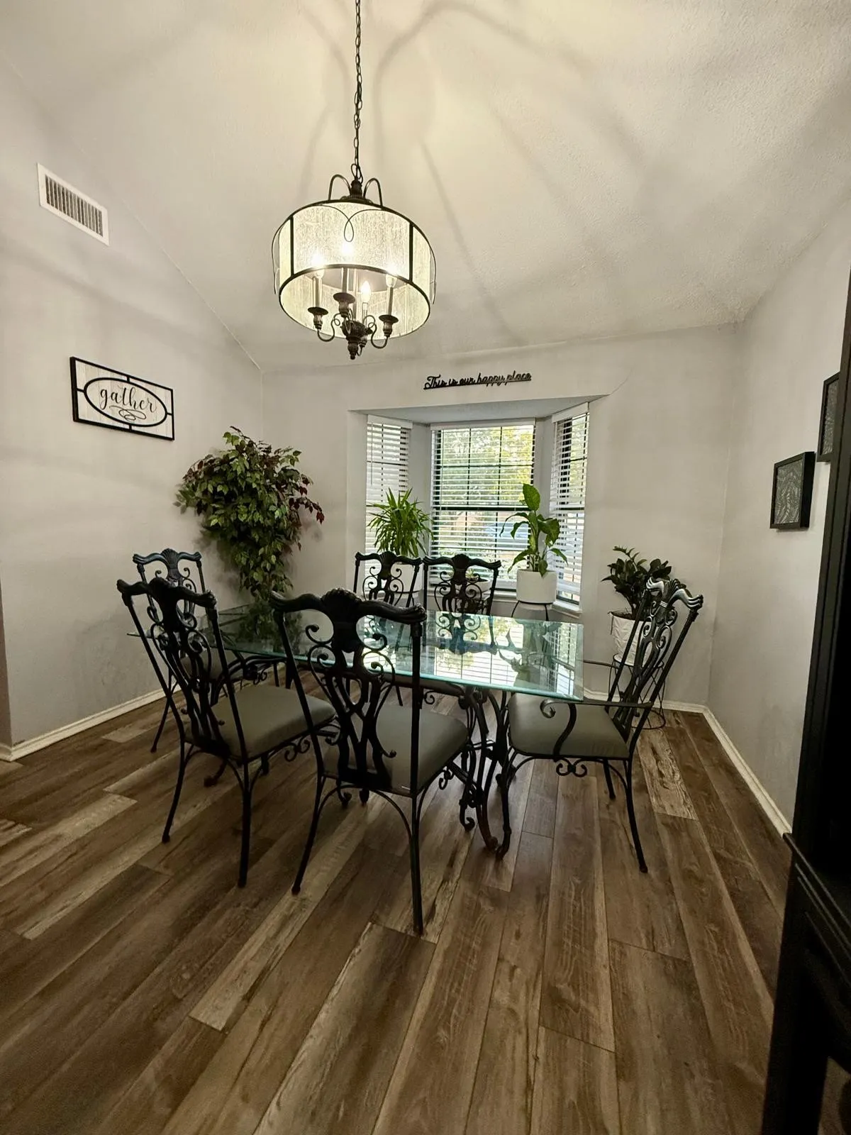 Wood-finish flooring, vaulted ceiling, bay window, chandelier light fixture, and horizontal window blinds