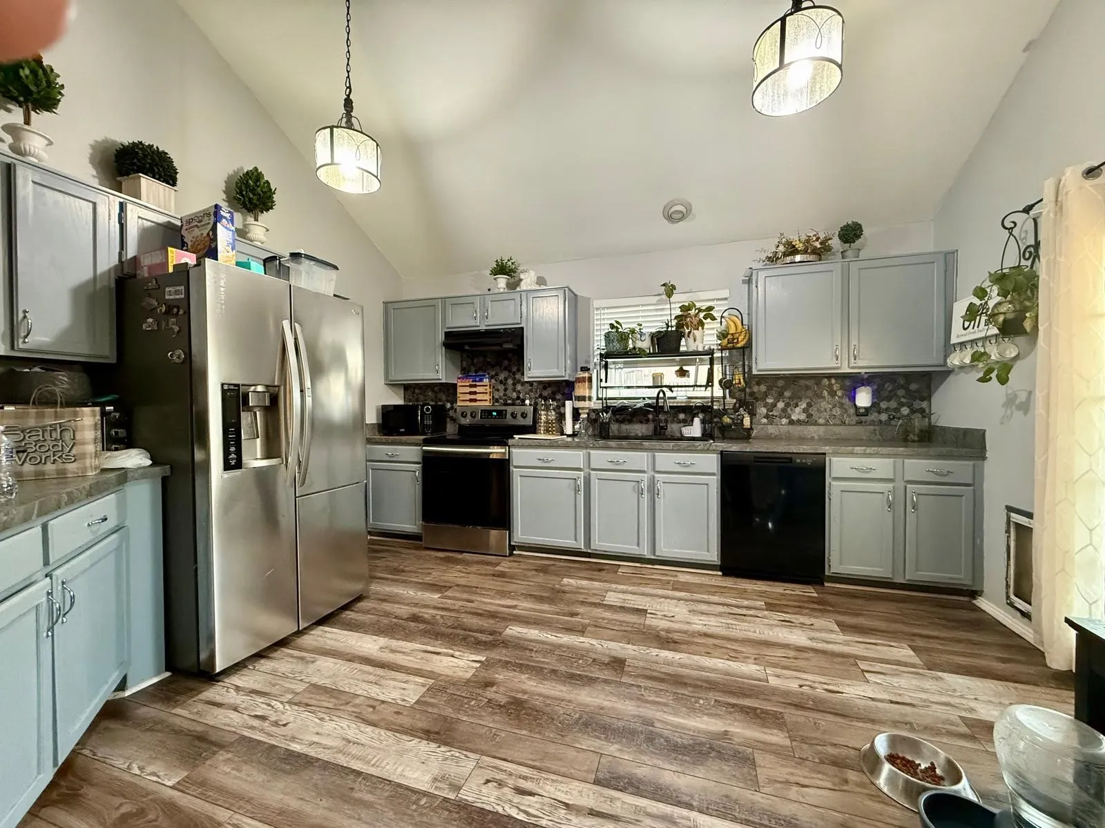 Kitchen featuring vaulted ceilings, wood-finish flooring, two pendant light fixtures, light-toned cabinetry, and a mosaic tile backsplash