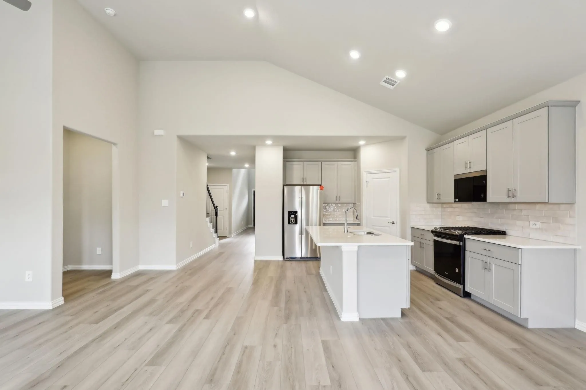 Open-concept living space with vaulted ceilings, wood-finish flooring, a kitchen island, stainless steel appliances, and light-toned cabinetry