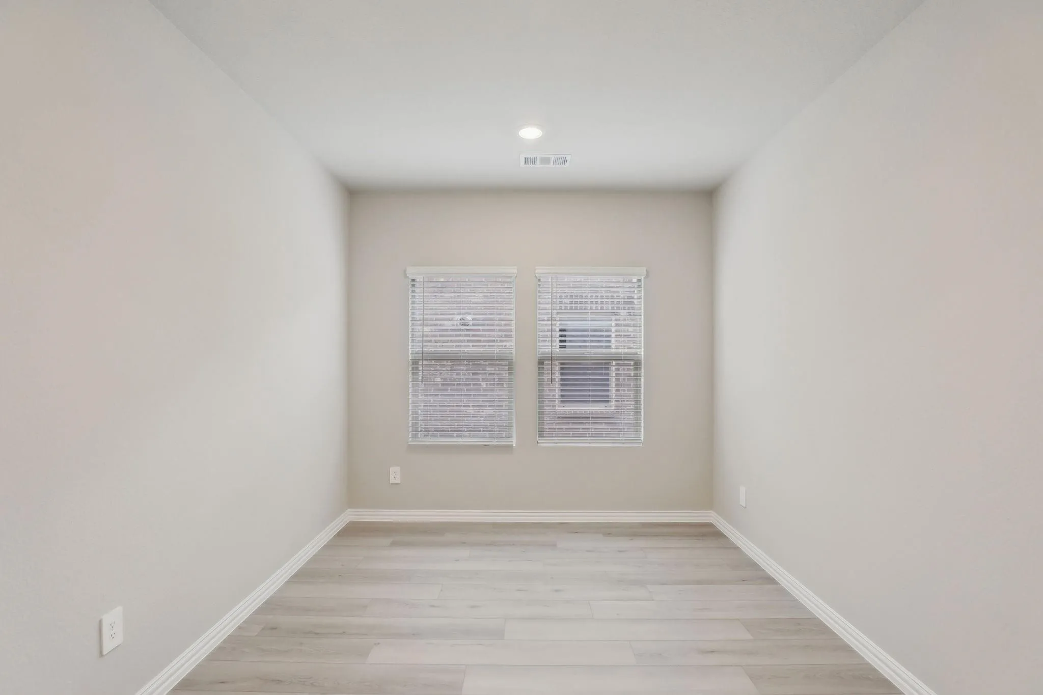 Light wood-finish flooring, recessed ceiling lighting, and two windows with blinds