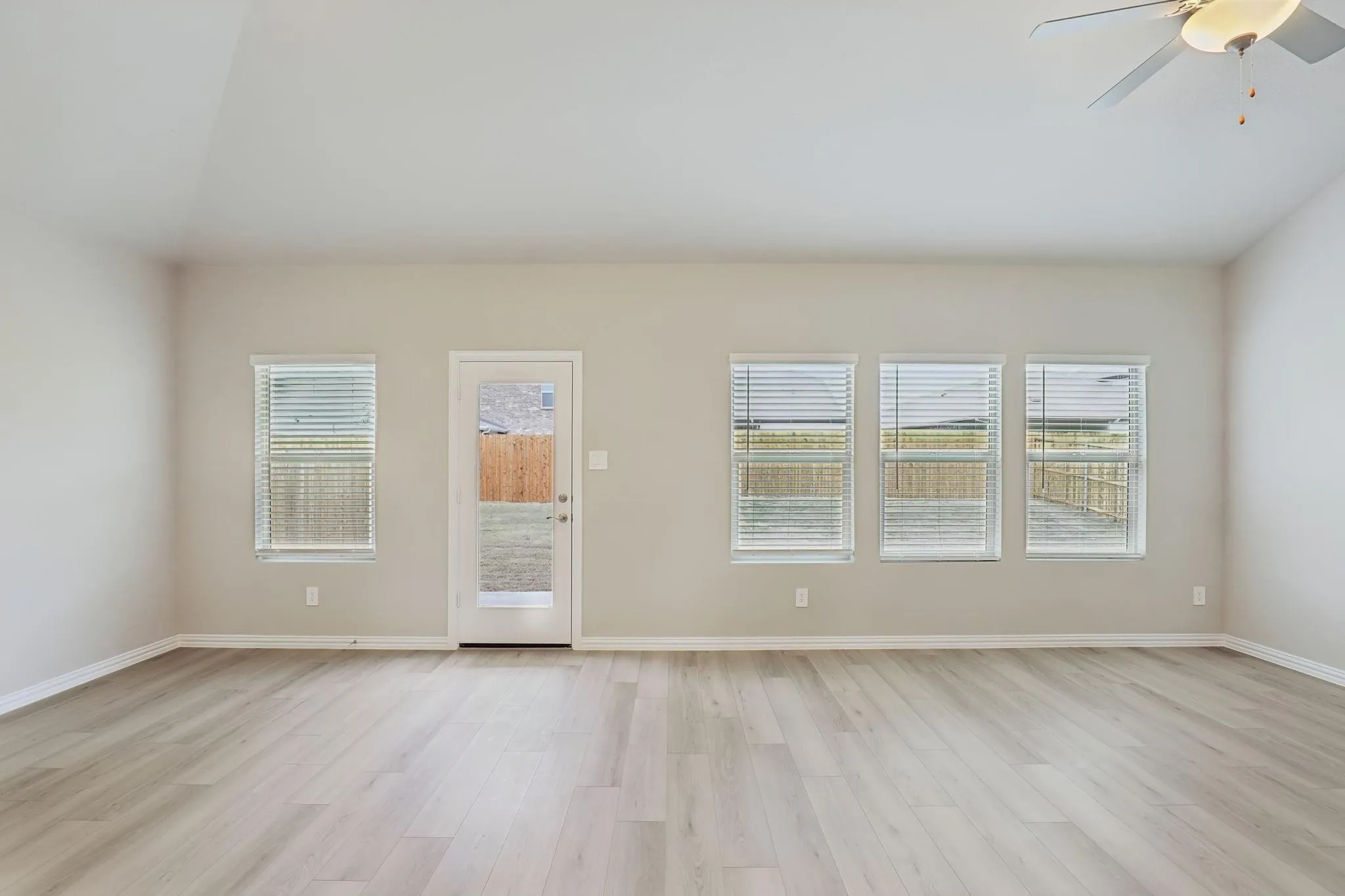 Vaulted ceiling with a ceiling fan, wood-finish flooring, multiple windows with blinds, and a glass-paneled exterior door