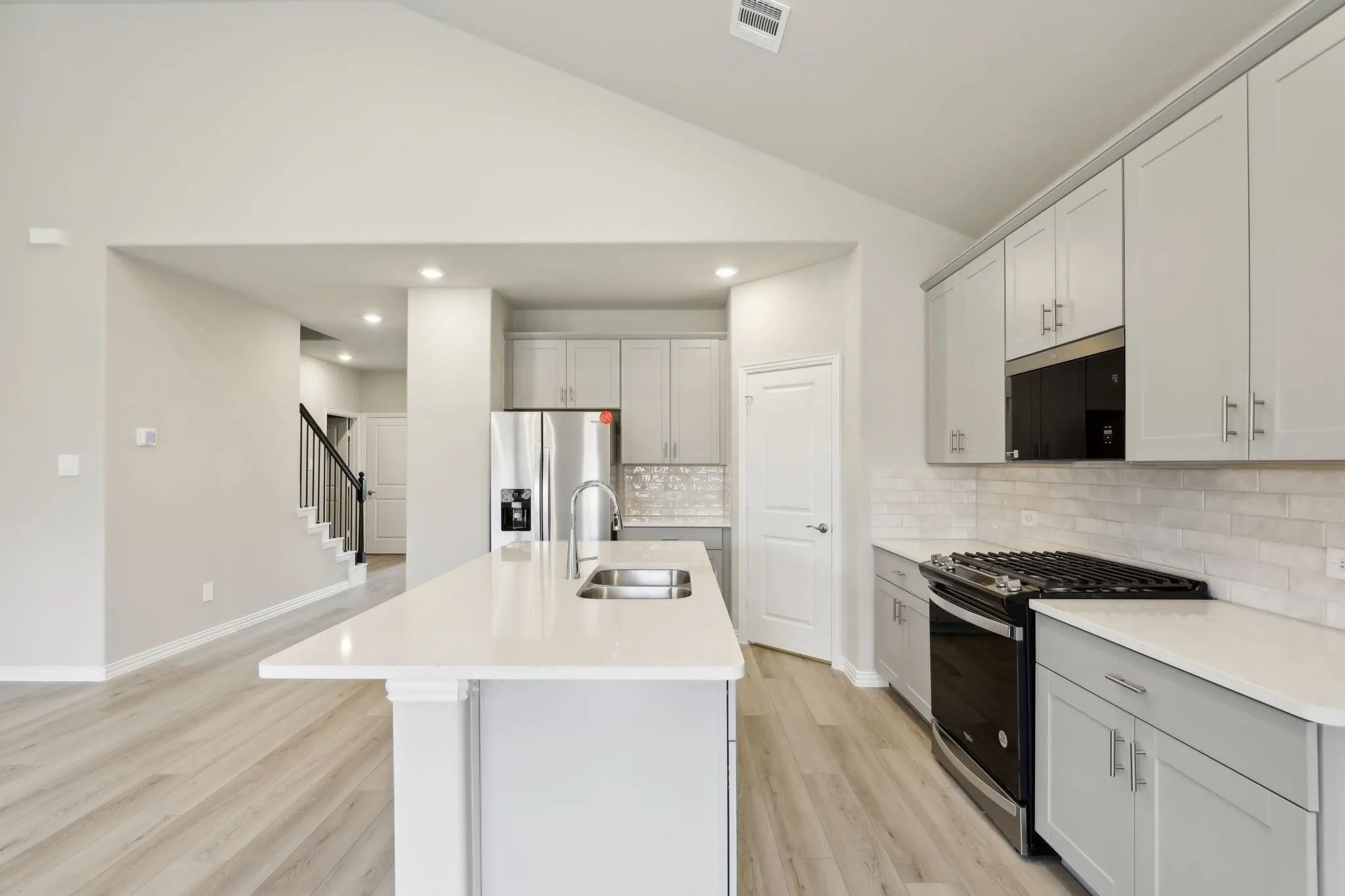 Kitchen featuring a vaulted ceiling, quartz countertops, stainless steel appliances, light gray cabinetry, and wood-finish flooring