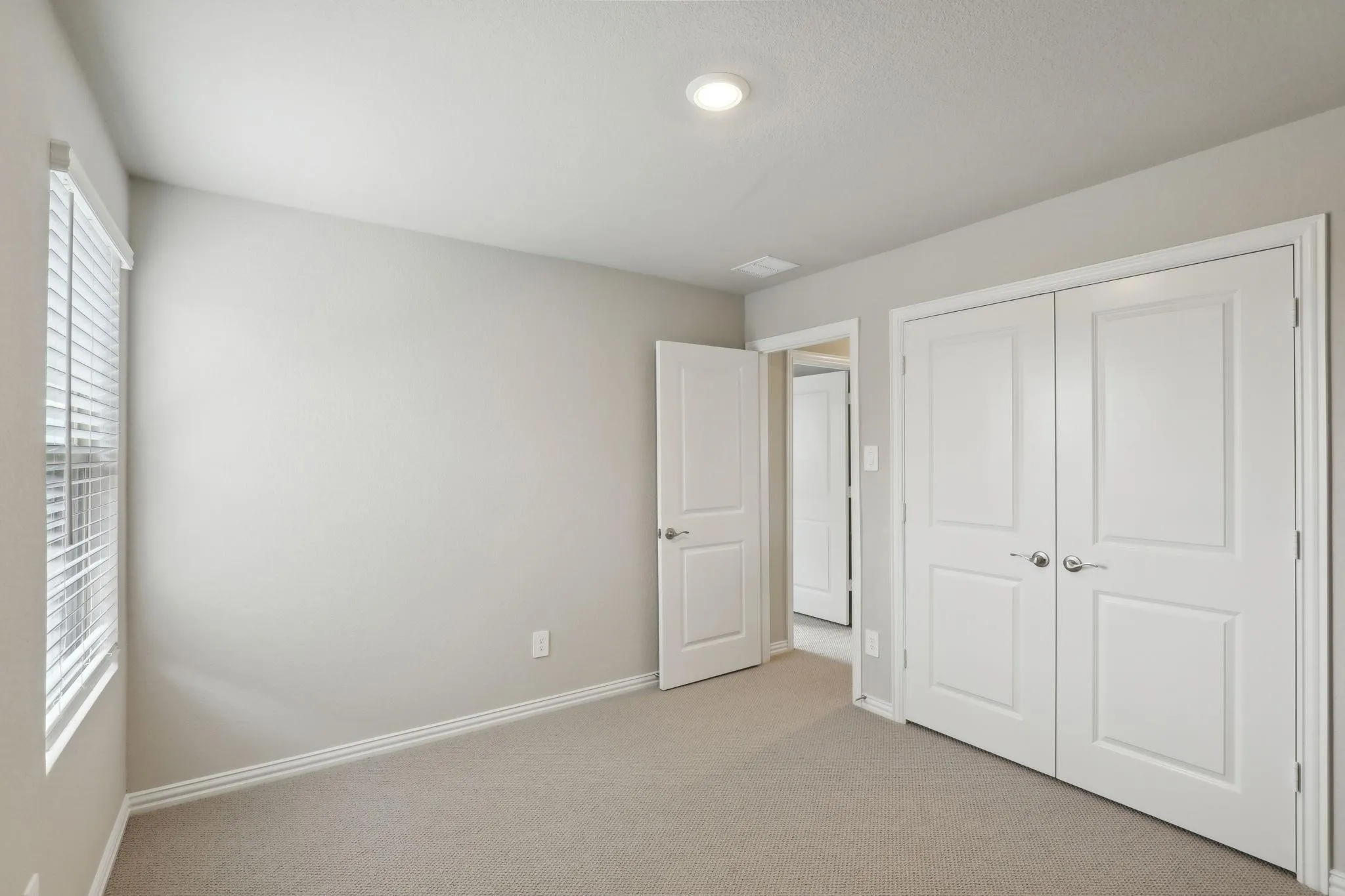Neutral tone wall paint, recessed ceiling lighting, carpeted flooring, window with horizontal blinds, and a double-door closet