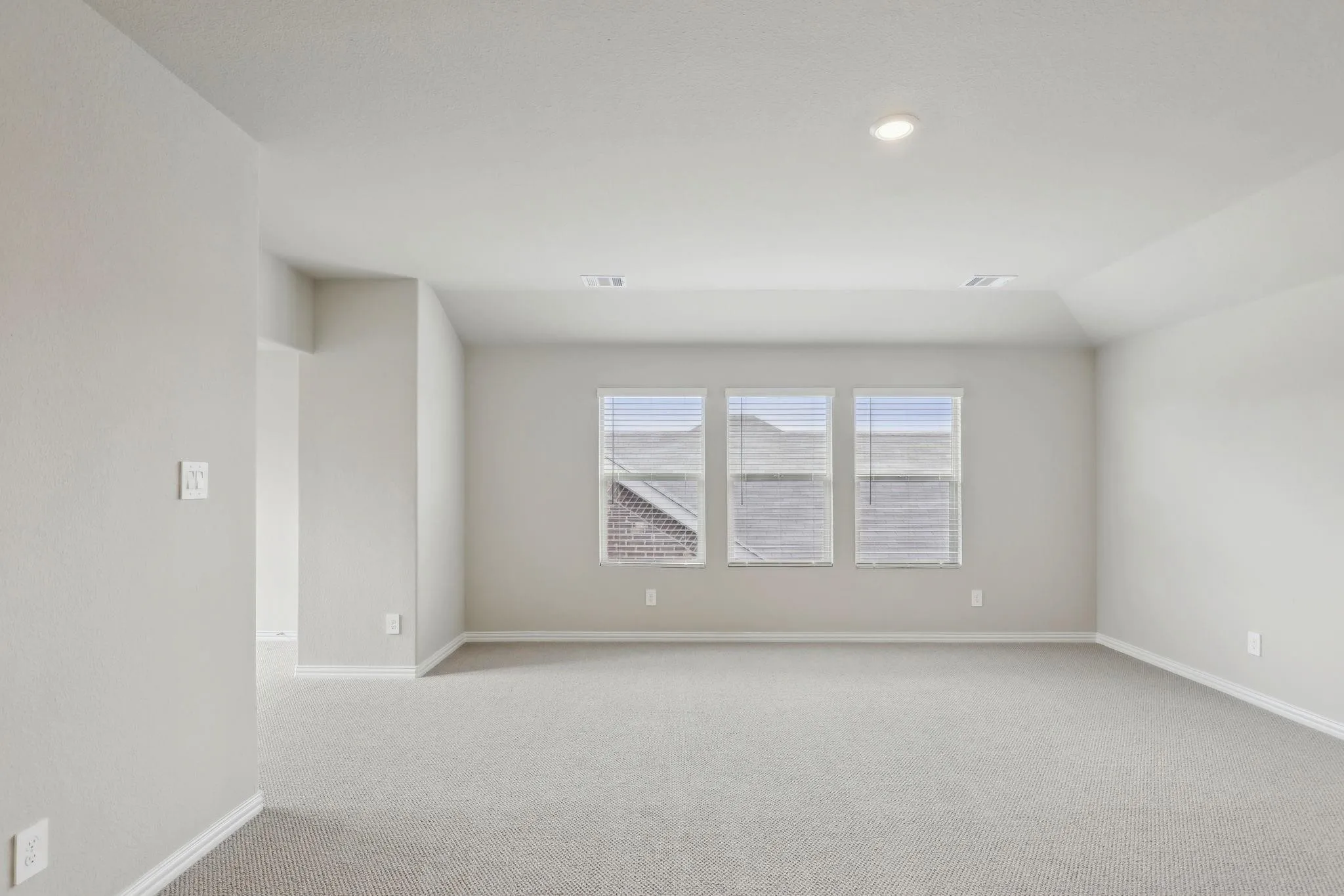 Recessed ceiling lighting, three windows with blinds, light-toned carpet flooring, neutral wall paint, and white trim