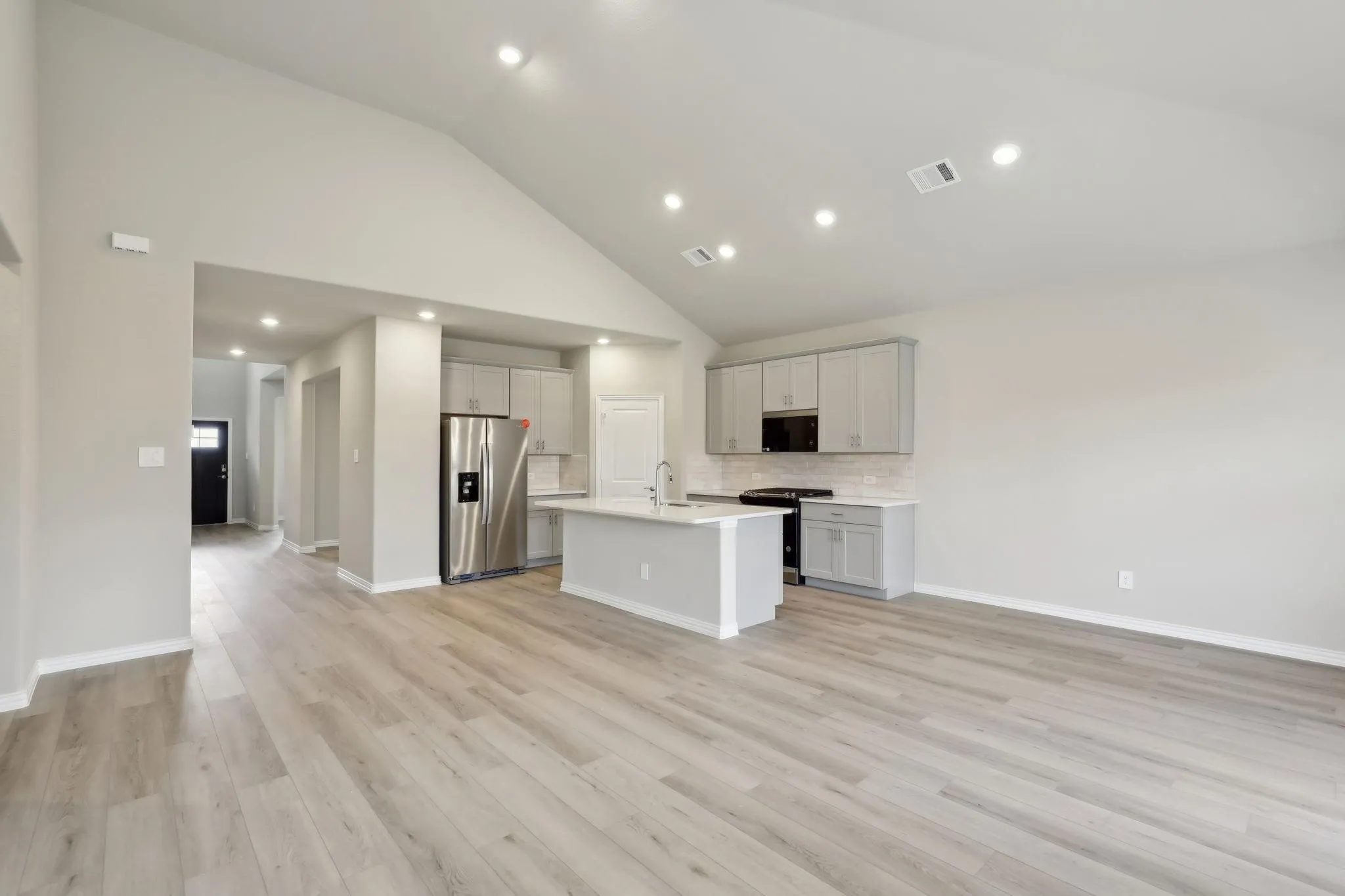 Vaulted ceiling with recessed lighting, wood-finish flooring, kitchen island with sink, stainless steel appliances, and subway tile backsplash