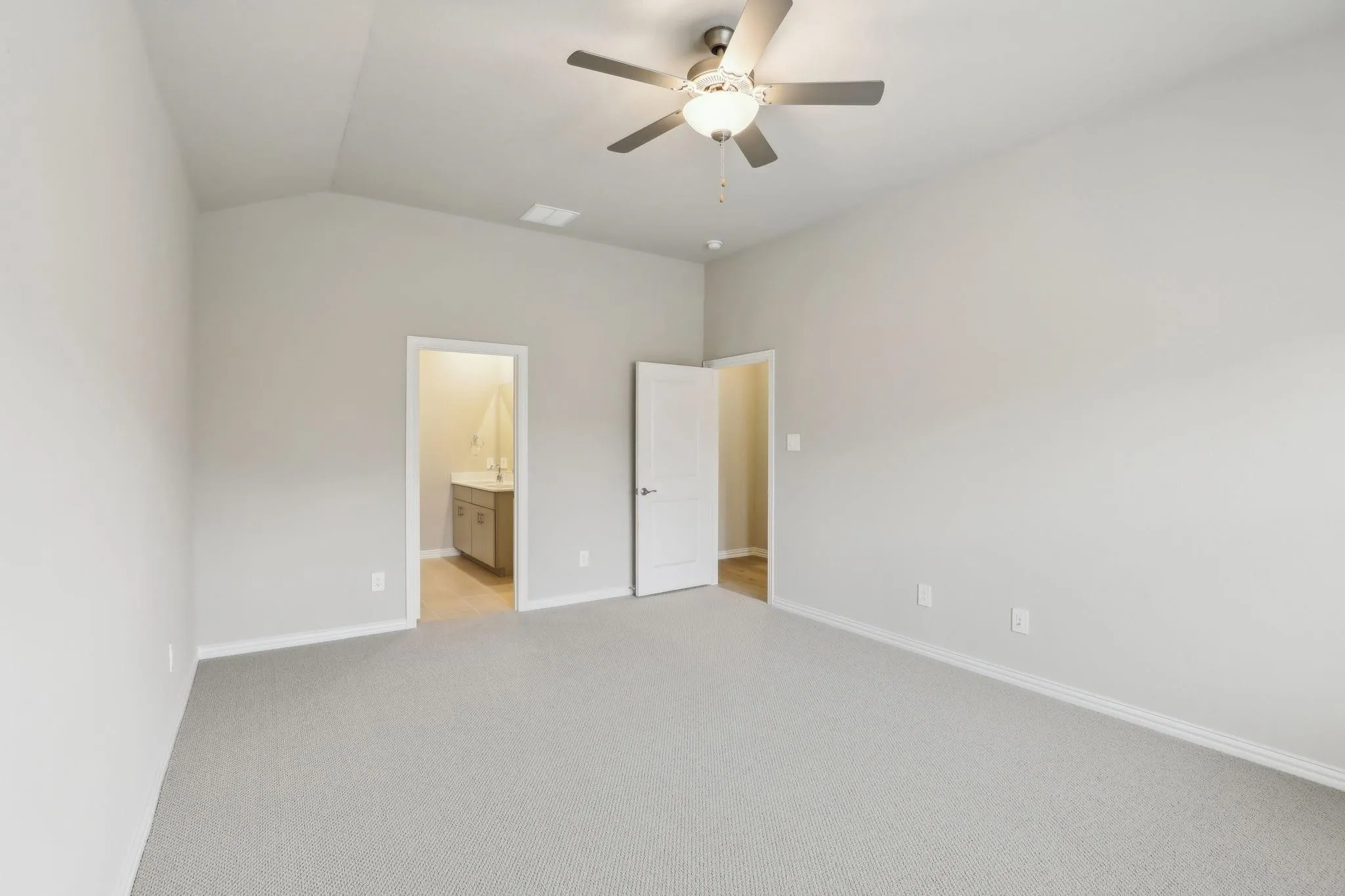 Vaulted ceiling, ceiling fan with integrated lighting, neutral wall paint, light gray carpet, interior door