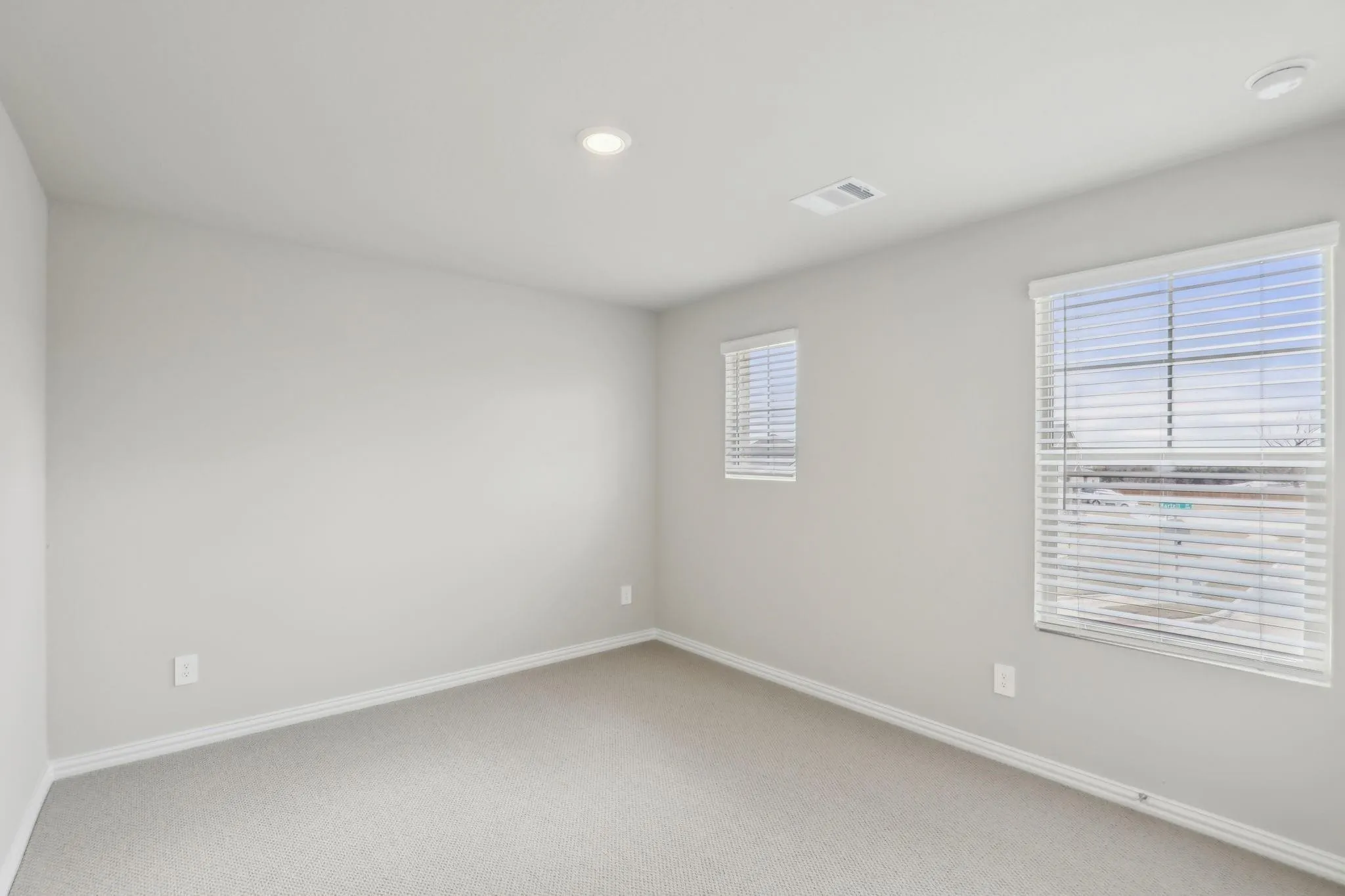Neutral wall paint, recessed lighting, two windows with blinds, and carpeting