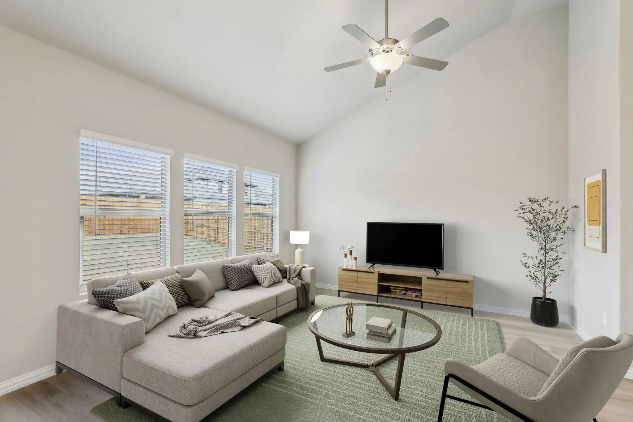 Vaulted ceiling, ceiling fan with integrated lighting, three windows with blinds, wood-finish flooring