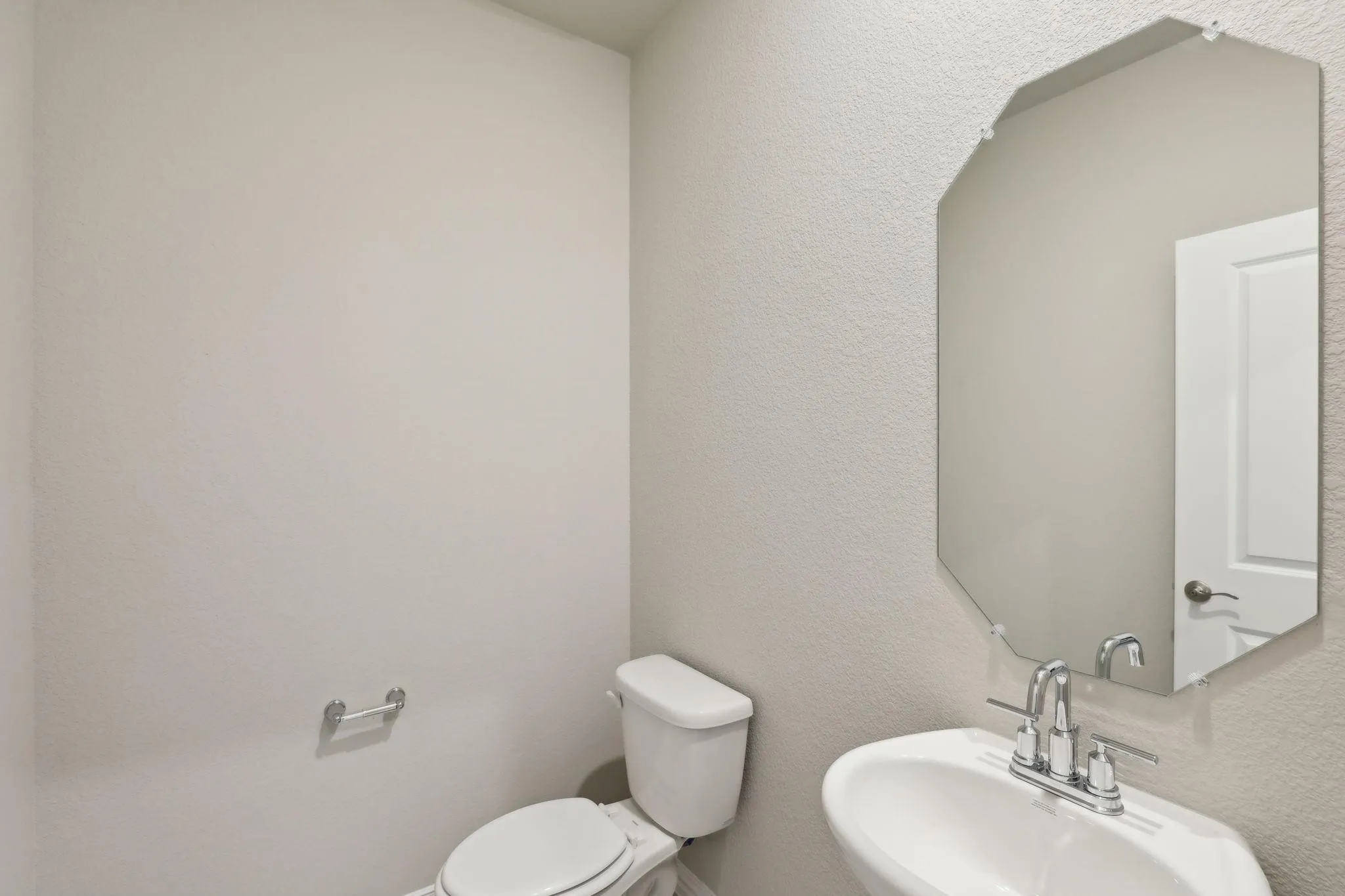 Pedestal sink with chrome faucet, beveled wall mirror, and white toilet