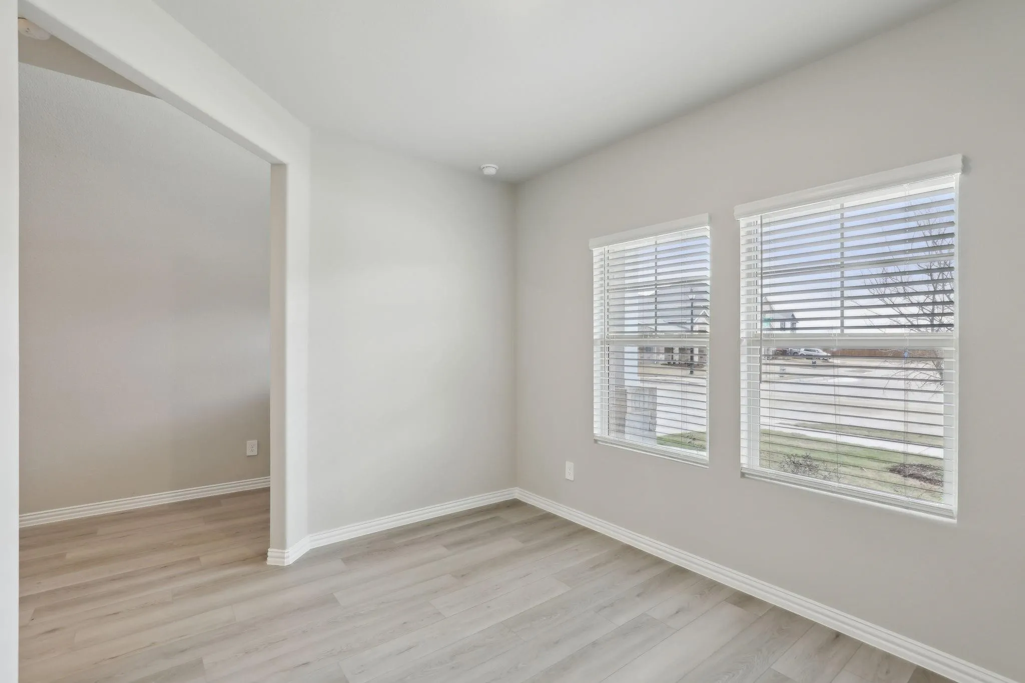 Light gray wall color, two windows with blinds, wood-finish flooring, and a wide doorway