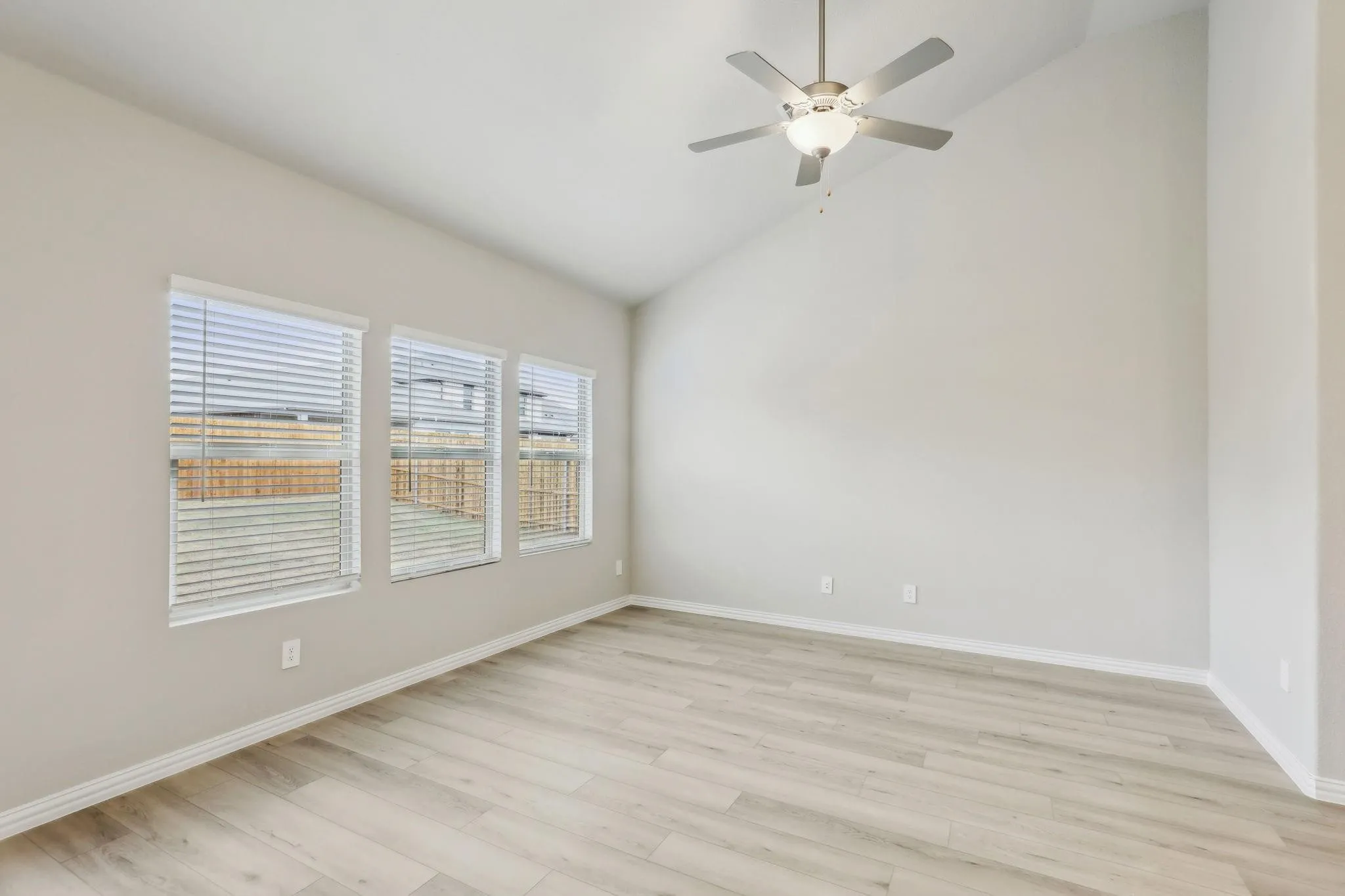 Vaulted ceiling with a ceiling fan, three windows with blinds, wood-finish flooring, and neutral wall tones