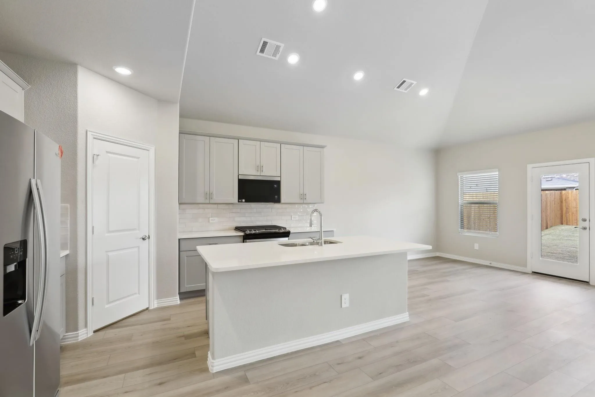 Contemporary kitchen with light wood-finish flooring, an island with an undermount sink, light gray cabinetry, a tile backsplash, and stainless steel appliances