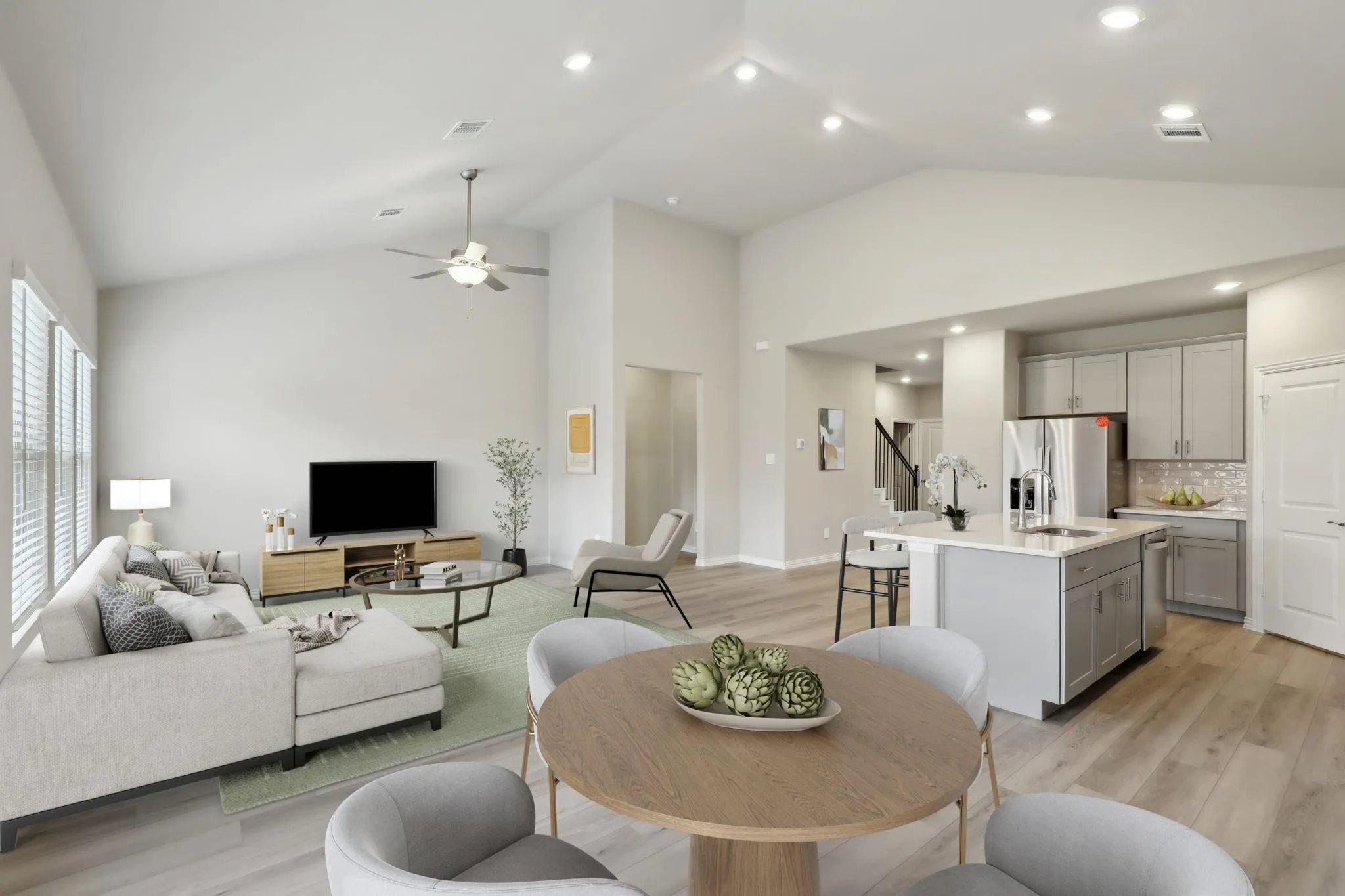 Vaulted ceilings with recessed lighting, wood-finish flooring, a kitchen island with an integrated sink, stainless steel appliances, and large windows with blinds