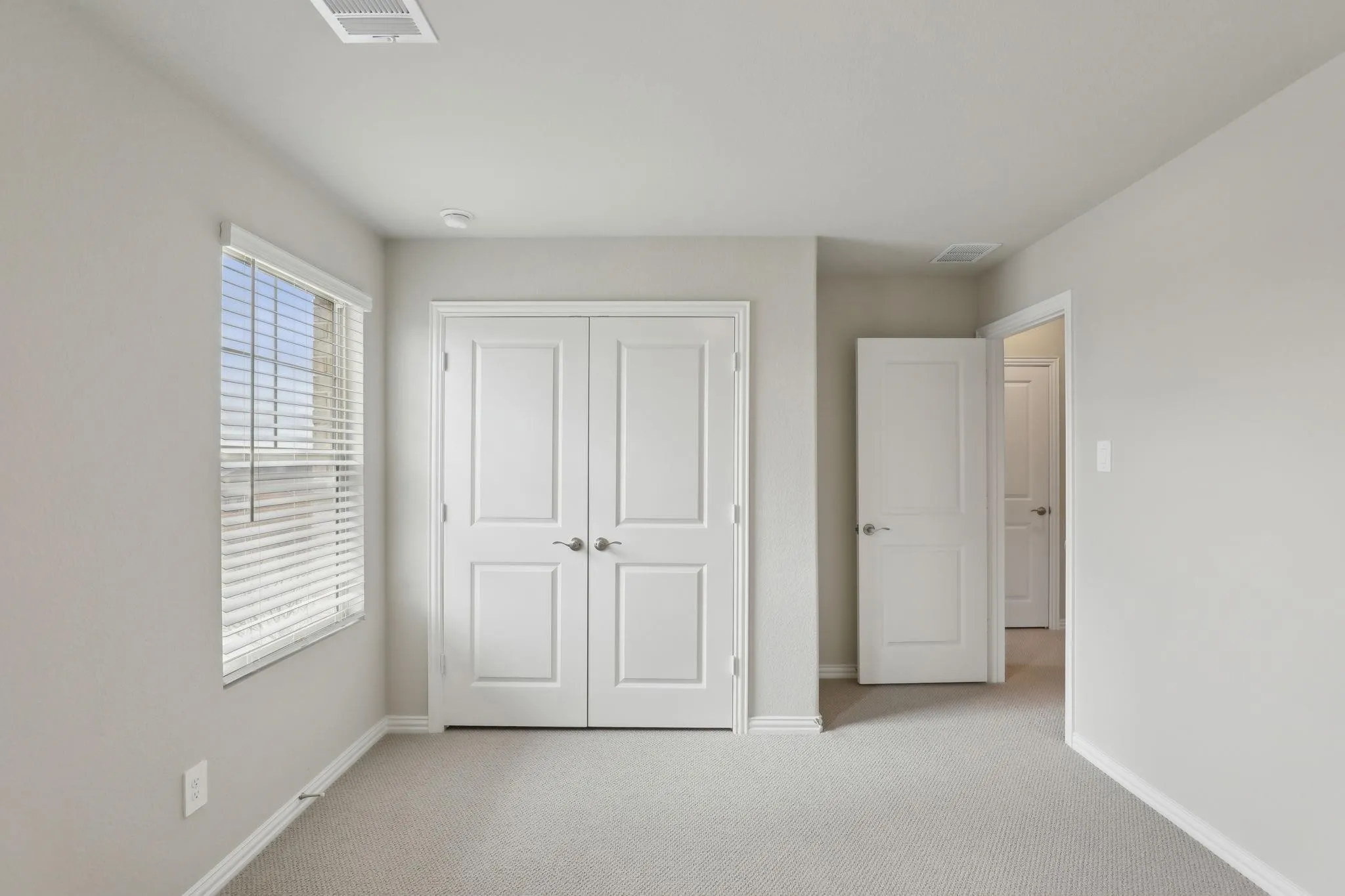 Neutral wall paint, light-colored carpet, double panel doors, recessed lighting, and a window with blinds