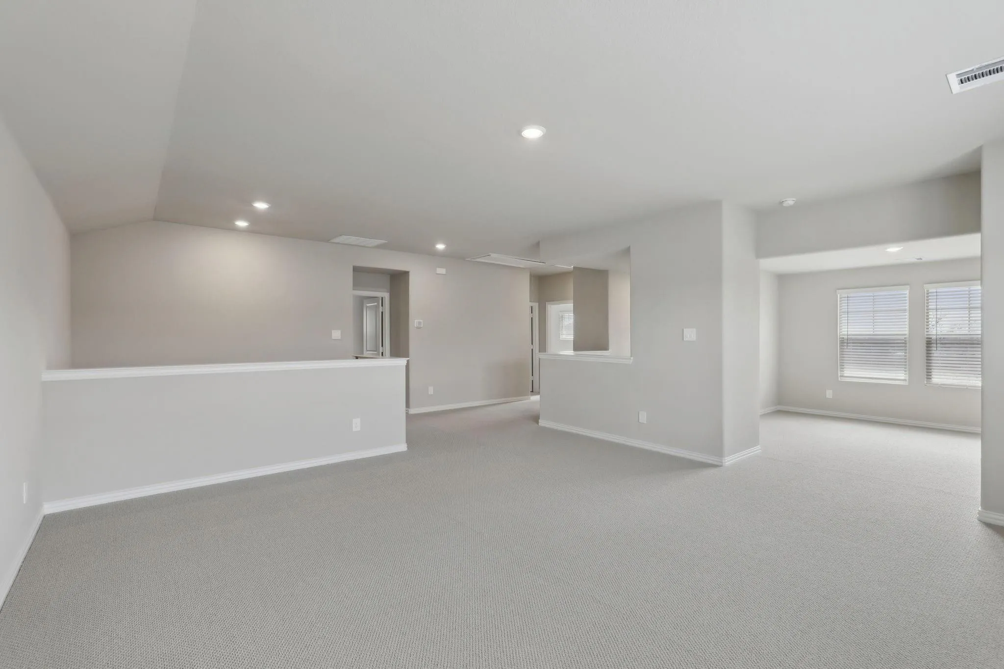 Spacious loft area featuring light gray carpeting, recessed lighting, and multiple windows