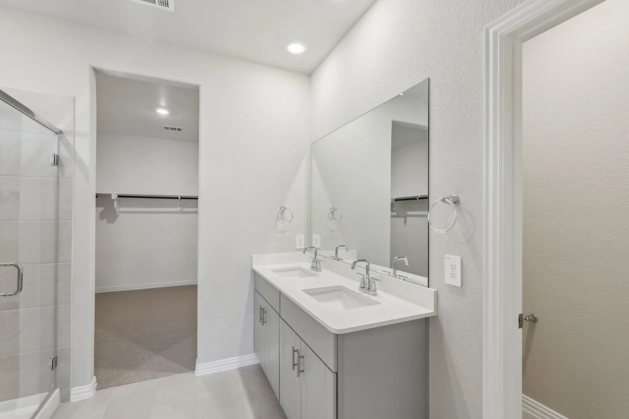 Dual sink vanity with stone-finish countertop, walk-in shower with glass enclosure, recessed lighting, and a walk-in closet with built-in shelving