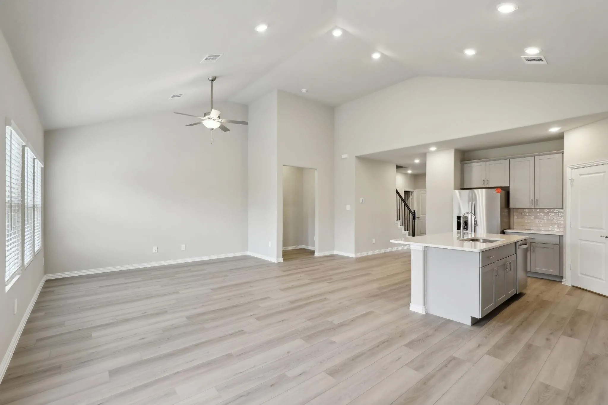 Vaulted ceiling with recessed lighting and ceiling fan, wood-finish flooring, kitchen island with sink and integrated dishwasher, gray cabinetry with subway tile backsplash, and stainless steel appliances