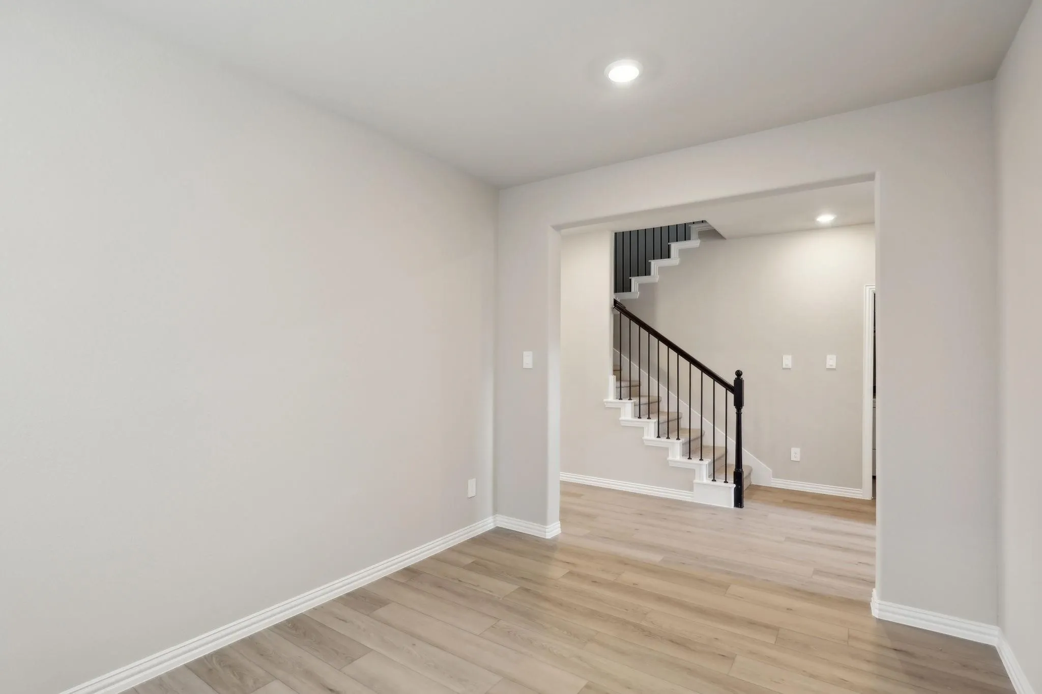 Recessed lighting, light-toned walls, wood-finish flooring, staircase with black metal balusters, and white risers