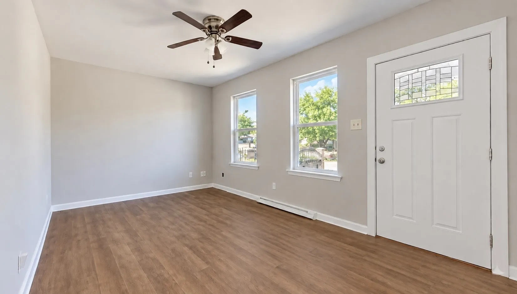 Wood-finish flooring, neutral wall tones, two windows with white trim, a decorative glass entry door, and a ceiling fan with integrated lighting