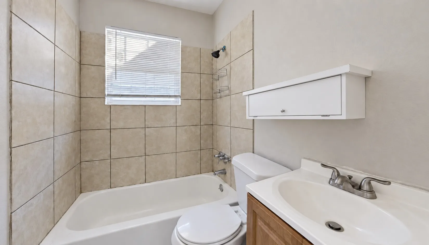 Bathtub with surrounding tile, wall-mounted medicine cabinet, vanity with integrated sink, and dual-handle faucet