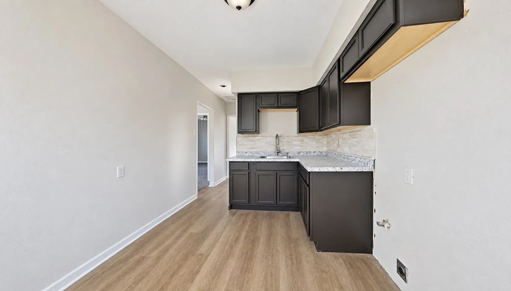 Kitchen with dark wood-finish cabinetry, light-toned countertops, a stainless steel sink, and a tiled backsplash