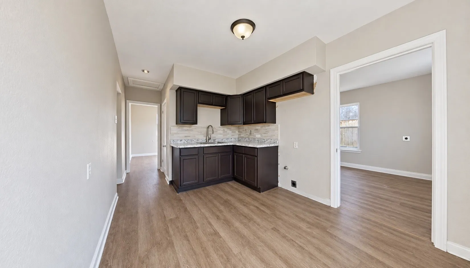 Kitchen area featuring dark wood-finish cabinetry, light stone-finish countertops, a tile backsplash, and a stainless-steel sink with a pull-down faucet