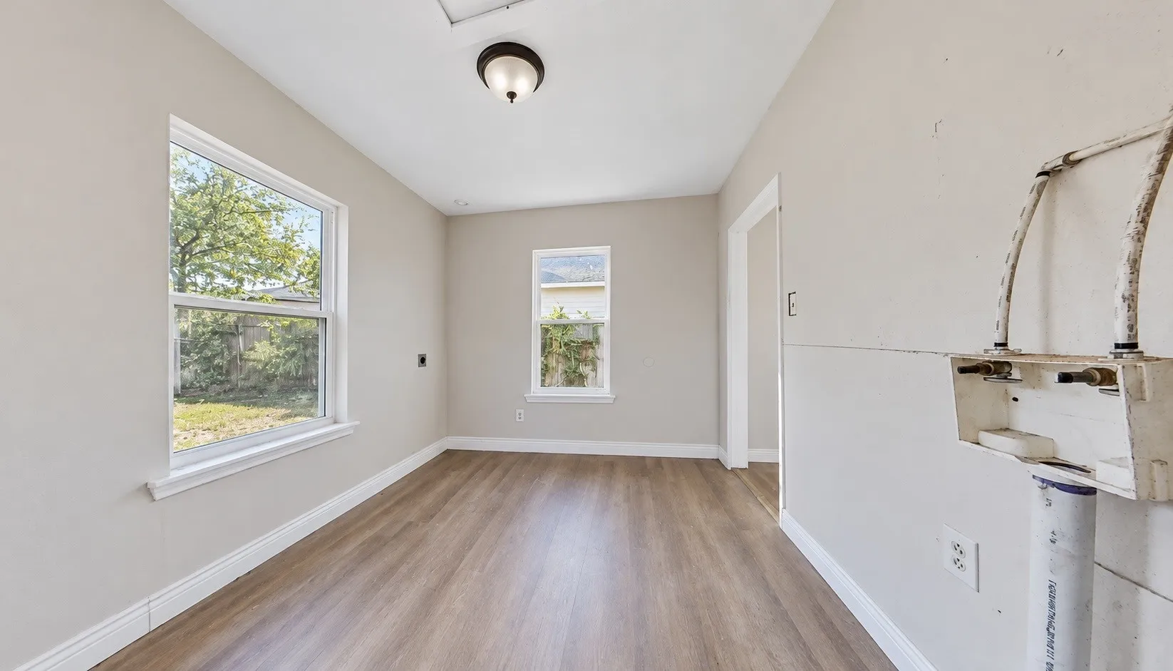 Wood-finish flooring with neutral wall tones, multiple windows, and overhead lighting