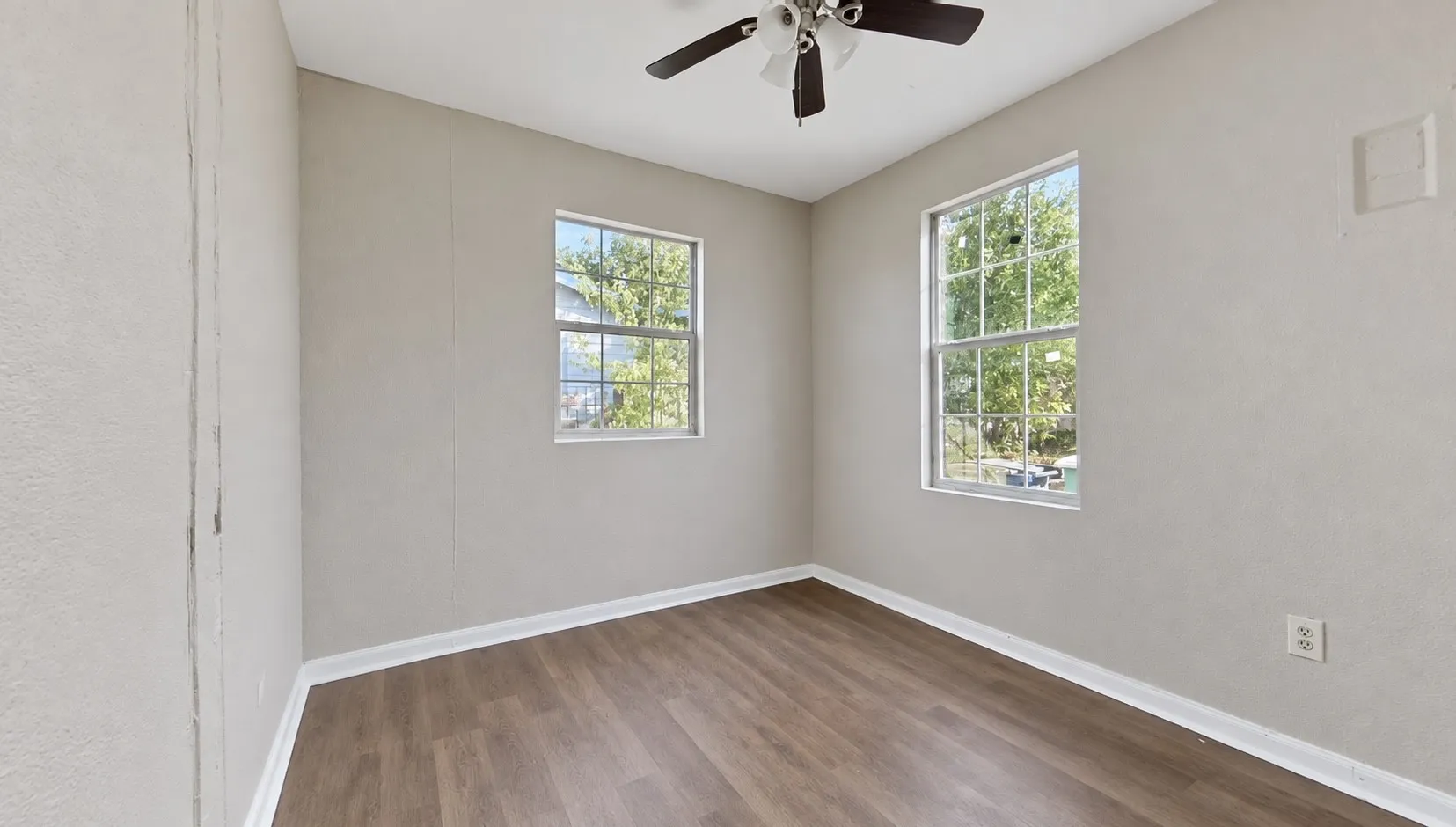 Wood-finish flooring, two large windows, white trim, and a ceiling fan with light fixture