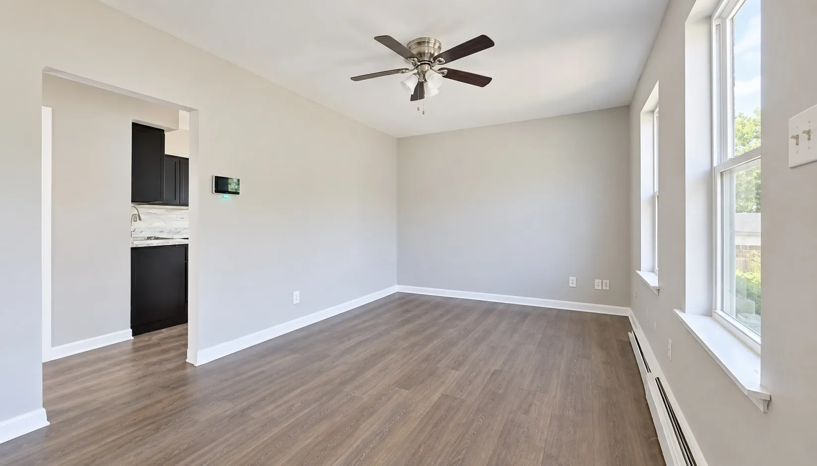 Spacious room featuring wood-finish flooring, light gray walls, a ceiling fan, and multiple windows