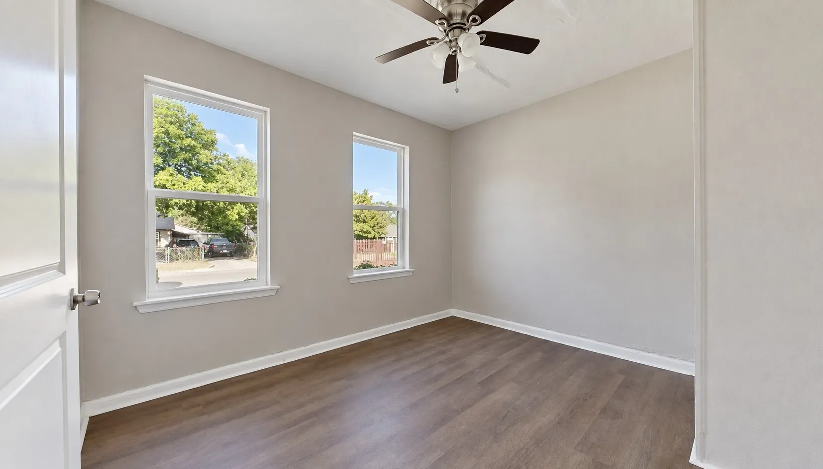 Wood-finish flooring, two large windows with white trim, and a ceiling fan with integrated lighting