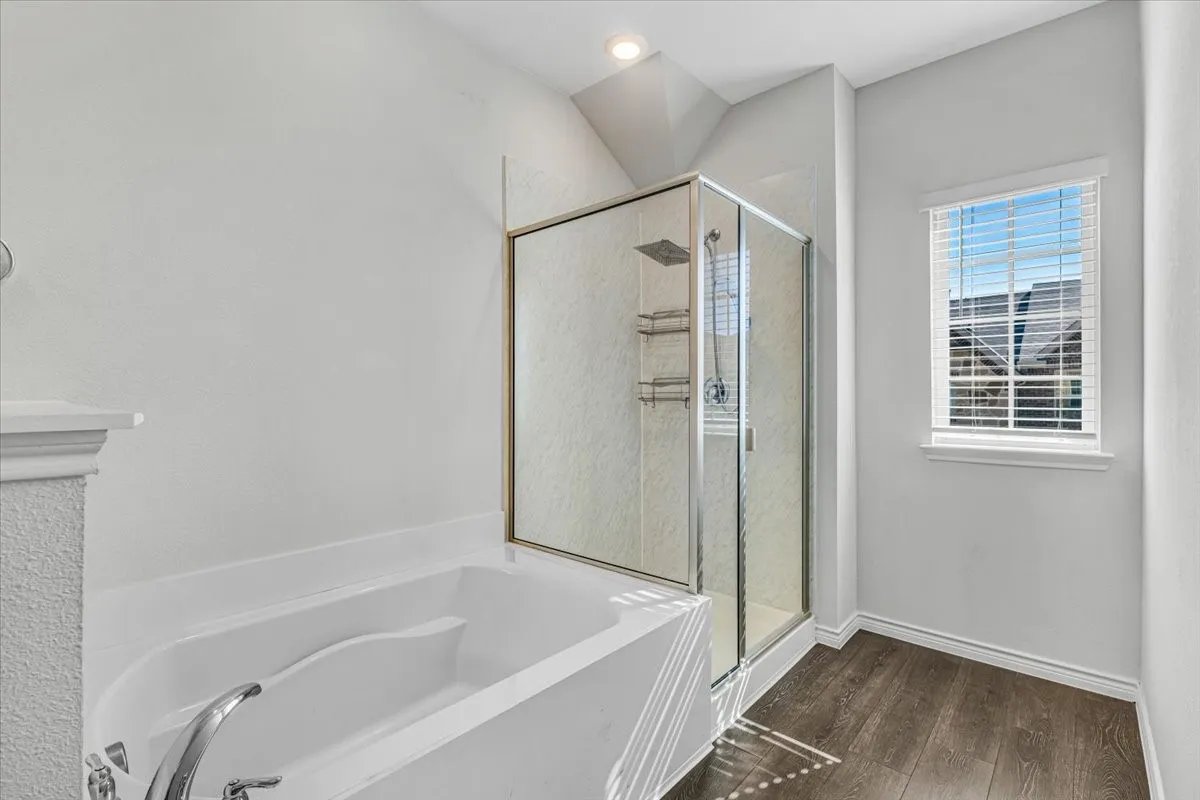 Built-in soaking tub with chrome fixtures, glass-enclosed shower with rain shower head, recessed lighting, and wood-finish flooring