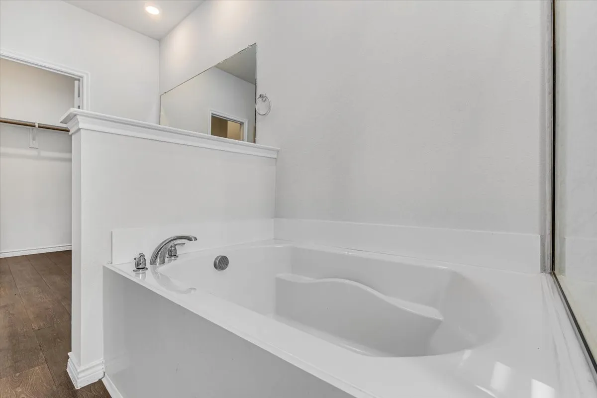 Built-in soaking tub with chrome fixtures, an adjacent walk-in closet, wood-finish flooring, and recessed lighting