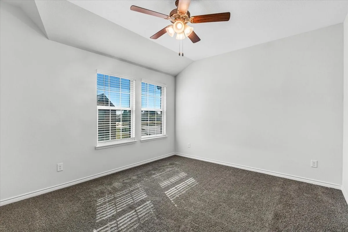 Vaulted ceiling with a ceiling fan light fixture, two windows with blinds, and carpeted​​‌​​​​‌​​‌‌​‌‌​​​‌‌​‌​‌​‌​​​‌​​ flooring