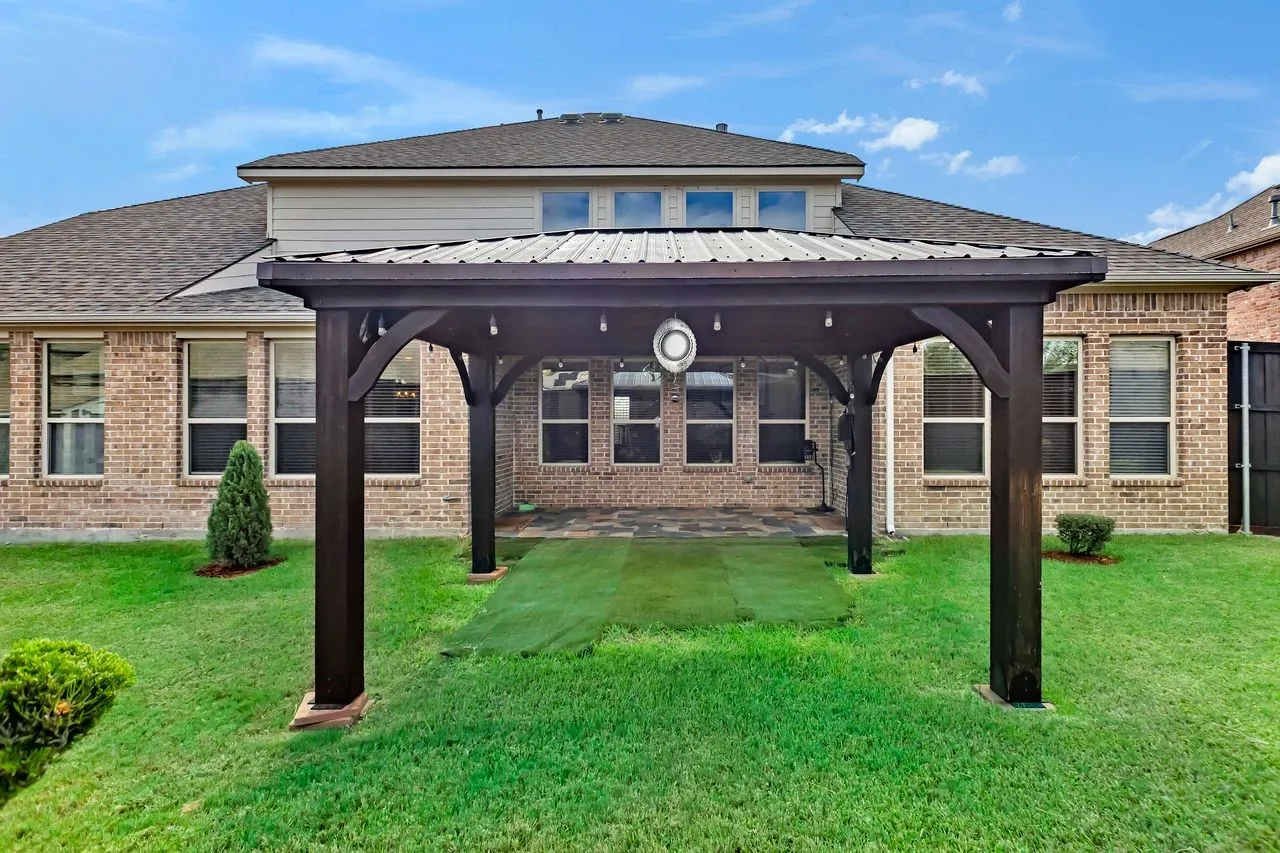 Expansive backyard featuring a wood pergola with metal roof, brick exterior, and multiple windows