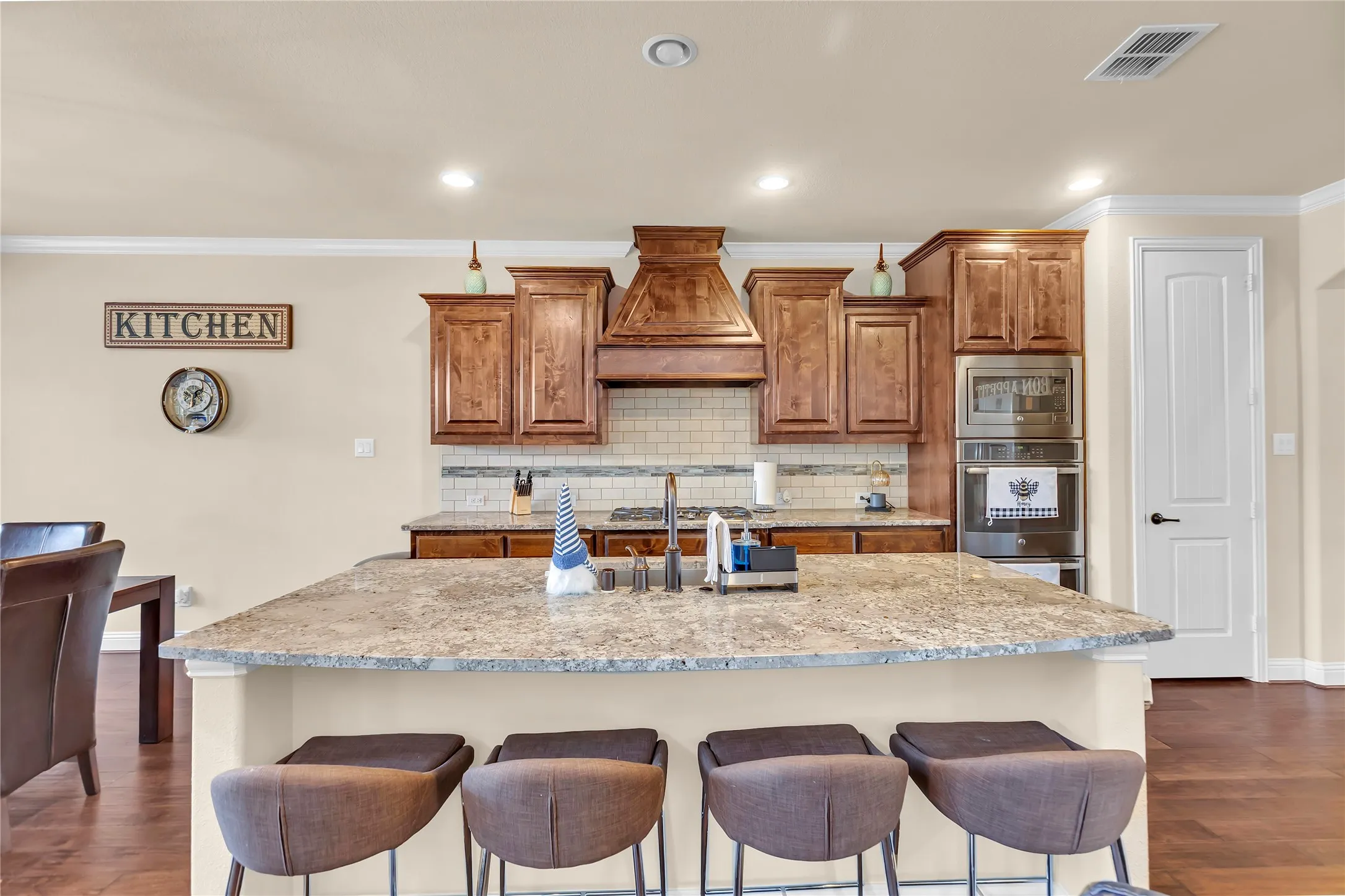 Wood-finish flooring with a large kitchen island, light-toned countertops, and built-in stainless steel appliances