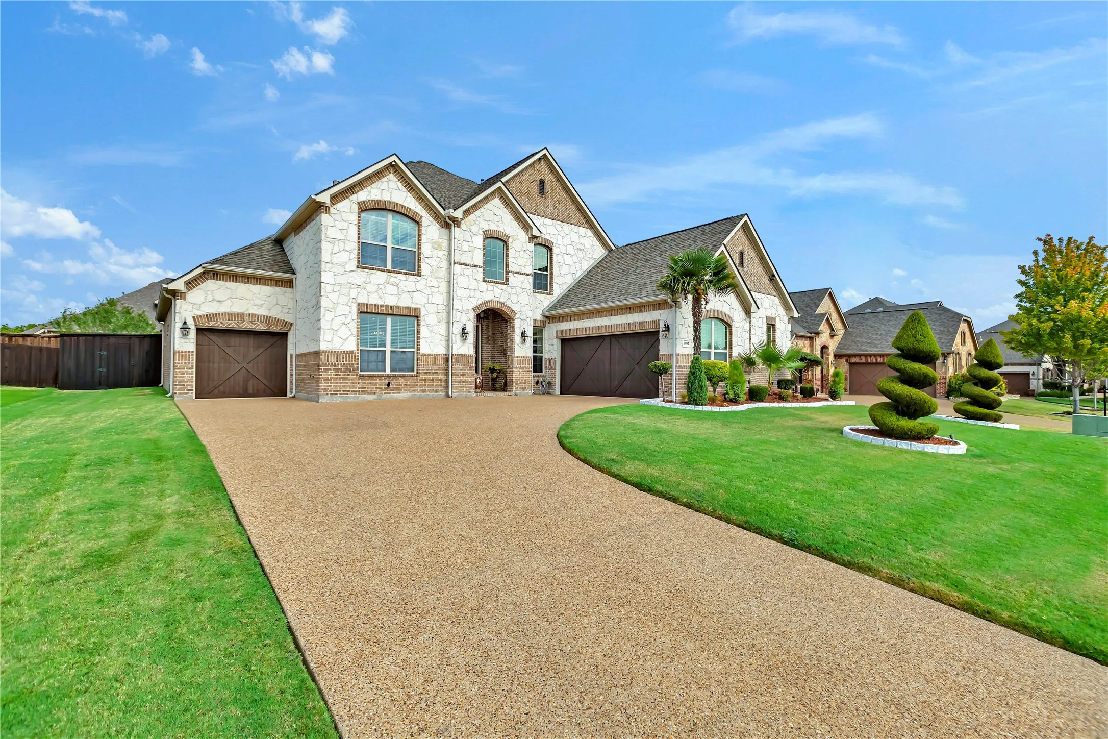 Two-story stone and brick exterior with multiple gables, arched entryways, and two wood-finish garage doors