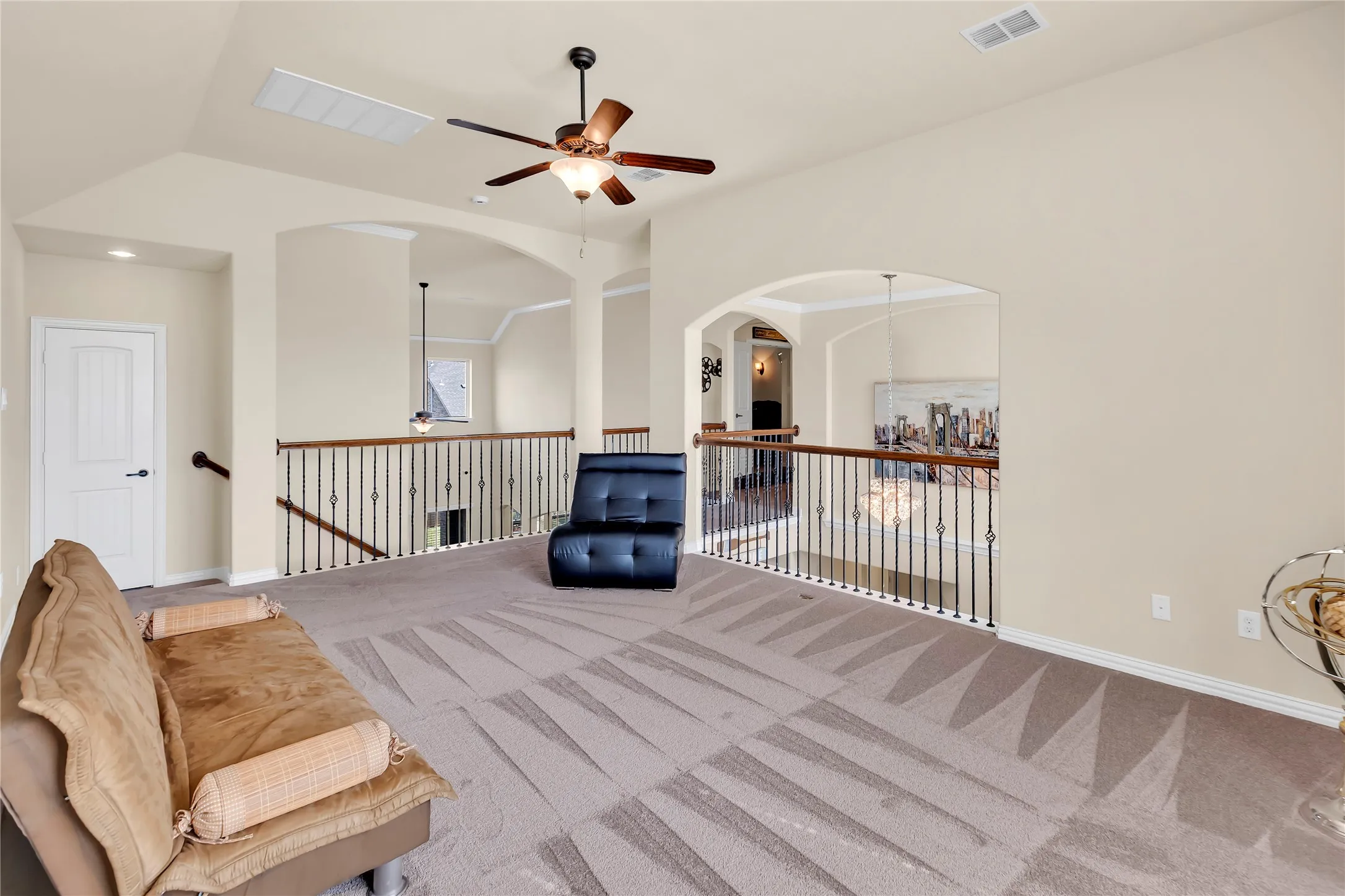 Spacious loft area with vaulted ceiling, ceiling fan, carpet flooring, arched doorways, and wrought iron balusters