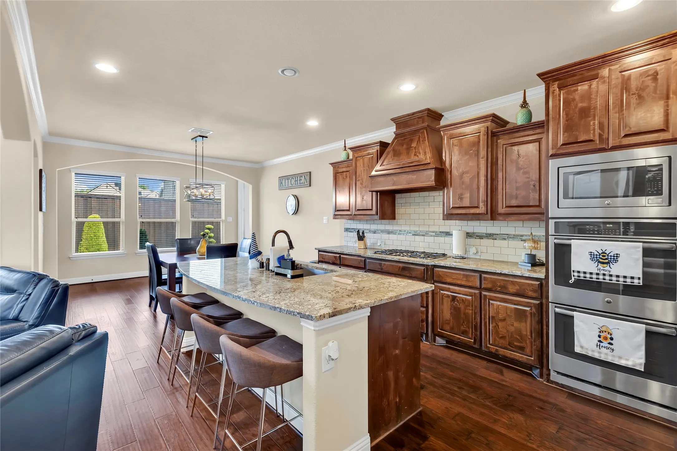 Kitchen featuring wood-finish flooring, a kitchen island with seating, built-in stainless steel appliances, granite countertops, and wood cabinetry