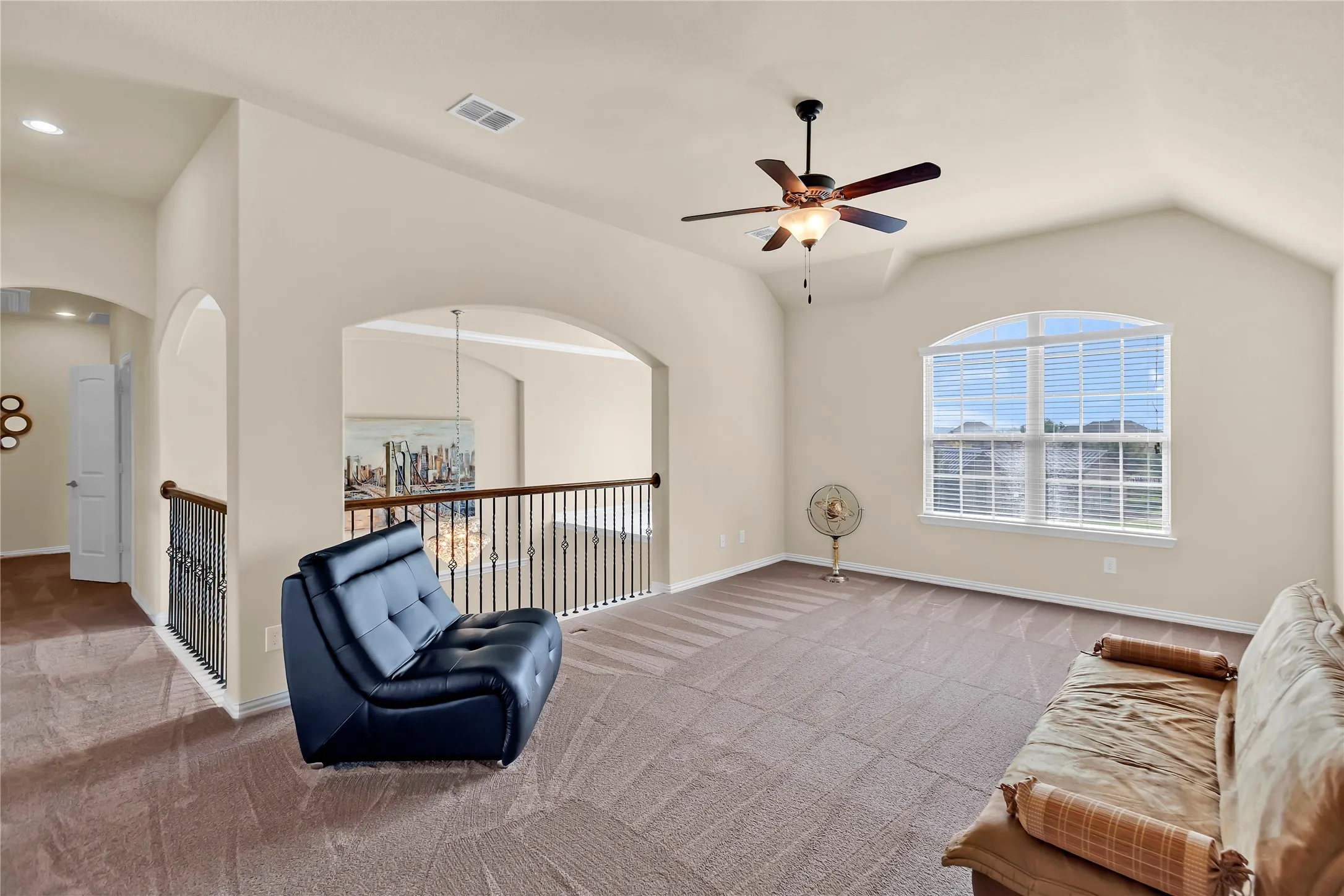 Spacious loft area featuring vaulted ceilings, an arched window with blinds, a ceiling fan, and wrought iron balusters