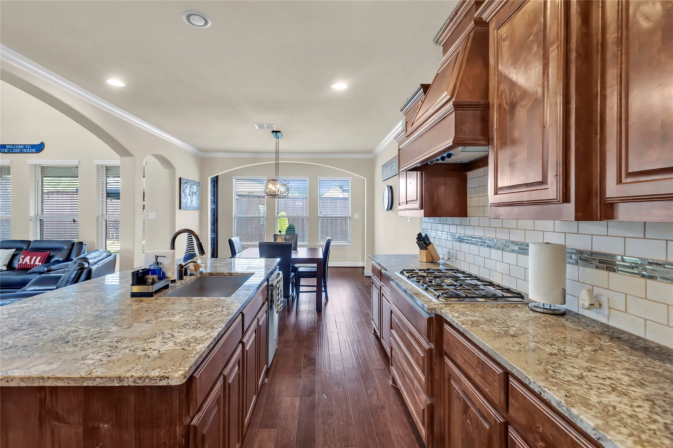 Kitchen featuring wood-finish flooring, granite countertops, a gas range, a built-in oven hood, and a subway tile backsplash
