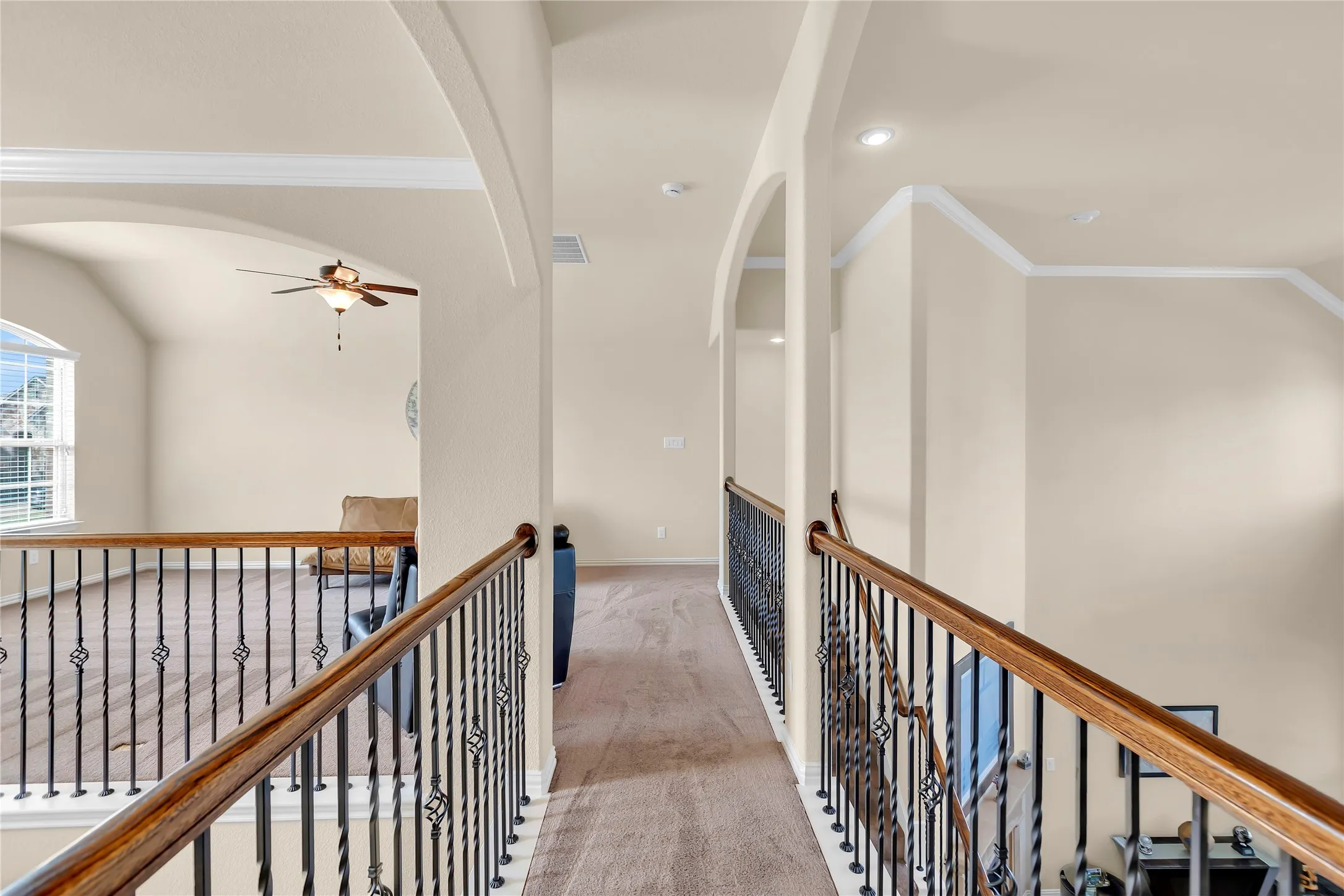 Second-level landing featuring wrought iron balusters with wood handrails, recessed lighting, crown molding, and arched doorways