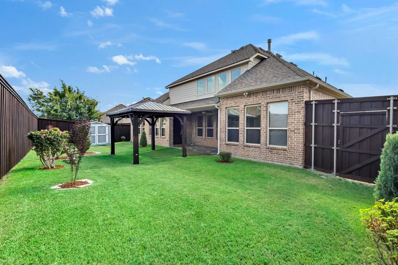 Expansive backyard featuring a gazebo, privacy fencing, a storage shed, and a brick exterior