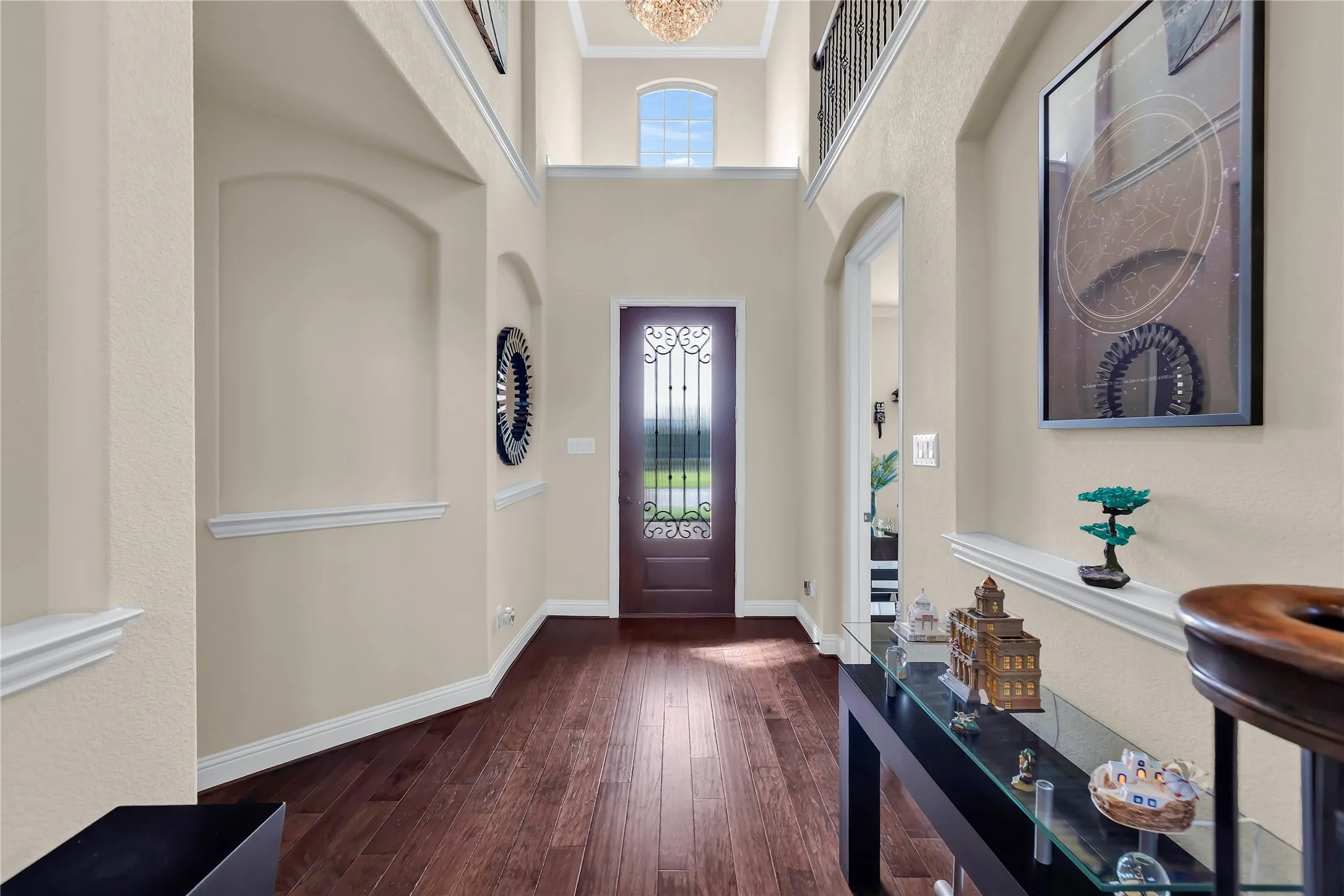 Two-story foyer featuring wood-finish flooring, an arched entryway, decorative wall niches, a wrought iron and glass front door, and an upper arched window