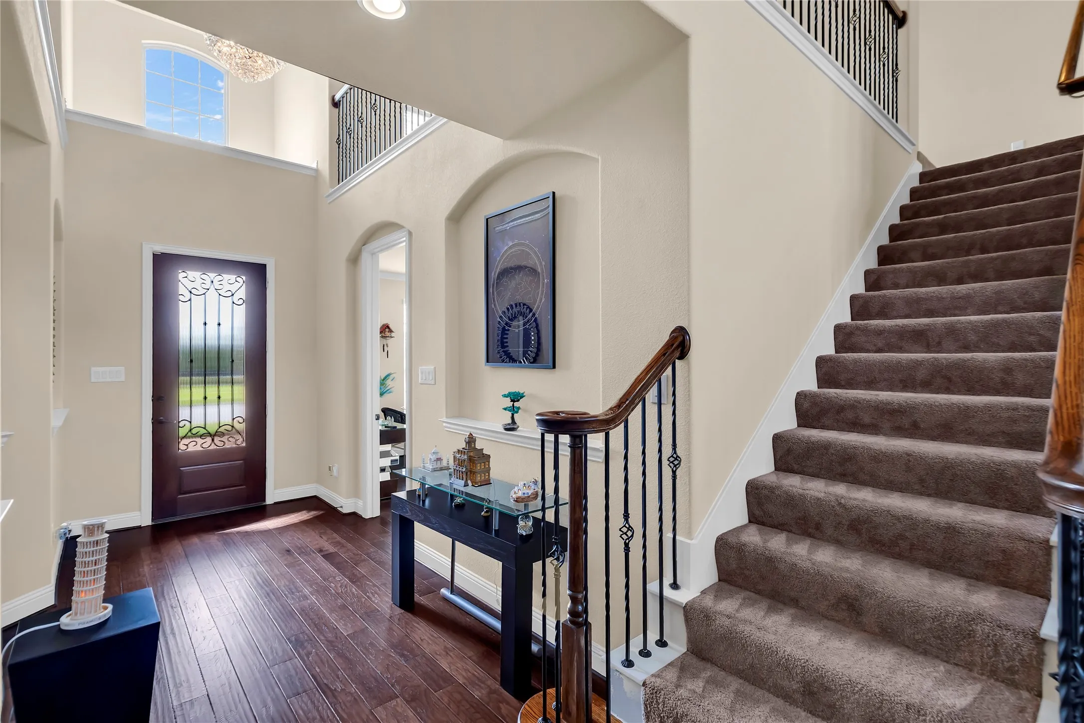 Two-story foyer with dark wood-finish flooring, wrought iron balusters, and a grand staircase with carpeted treads