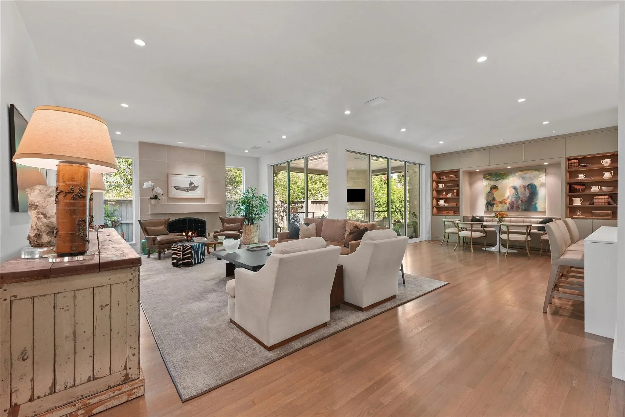Wood flooring connects the fireplace seating area to a dining nook with illuminated shelving and sliding glass doors overlook the covered patio.