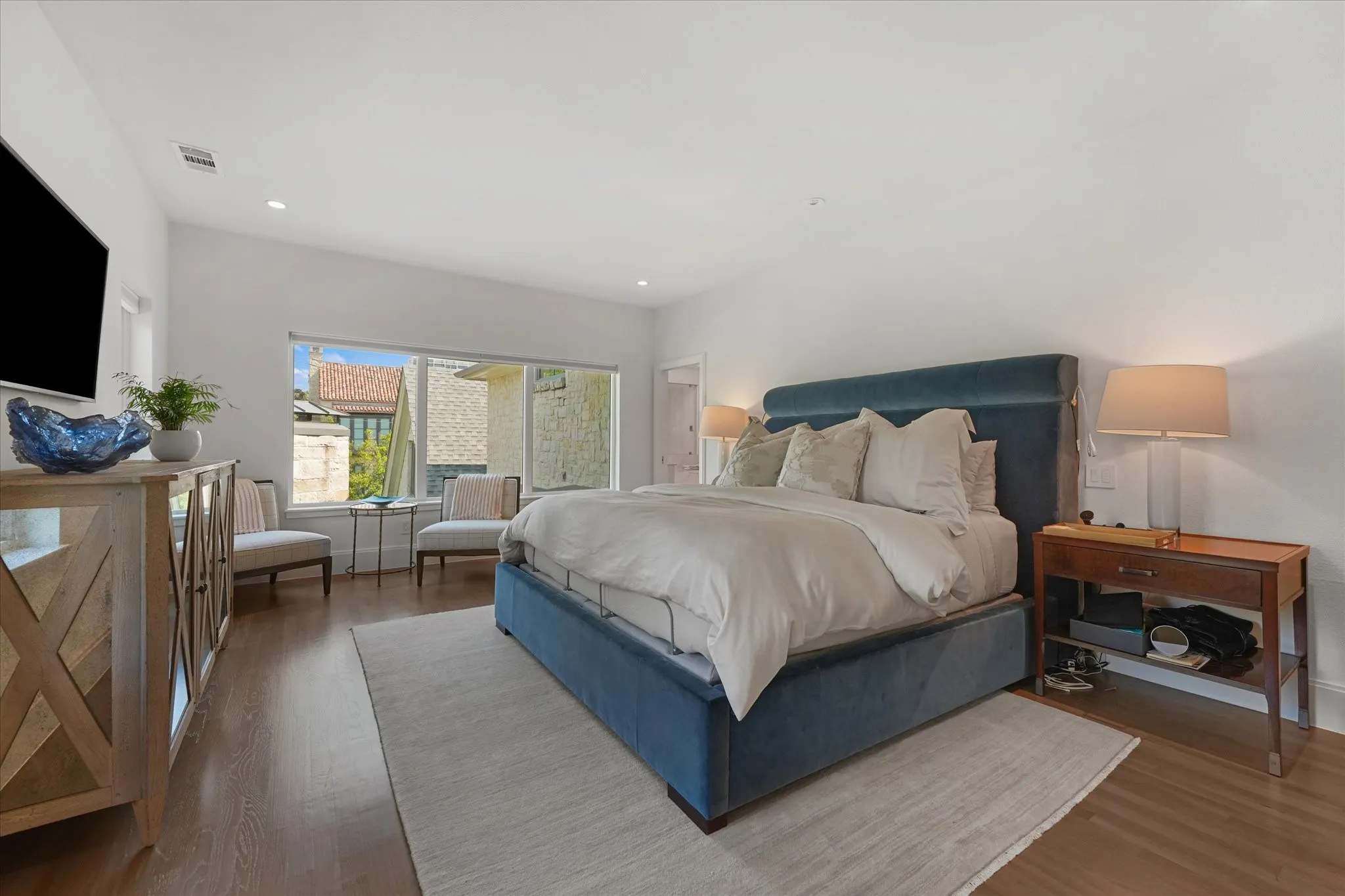A wide window brings daylight into a sitting area beside the bed, with wood flooring extending throughout the room.