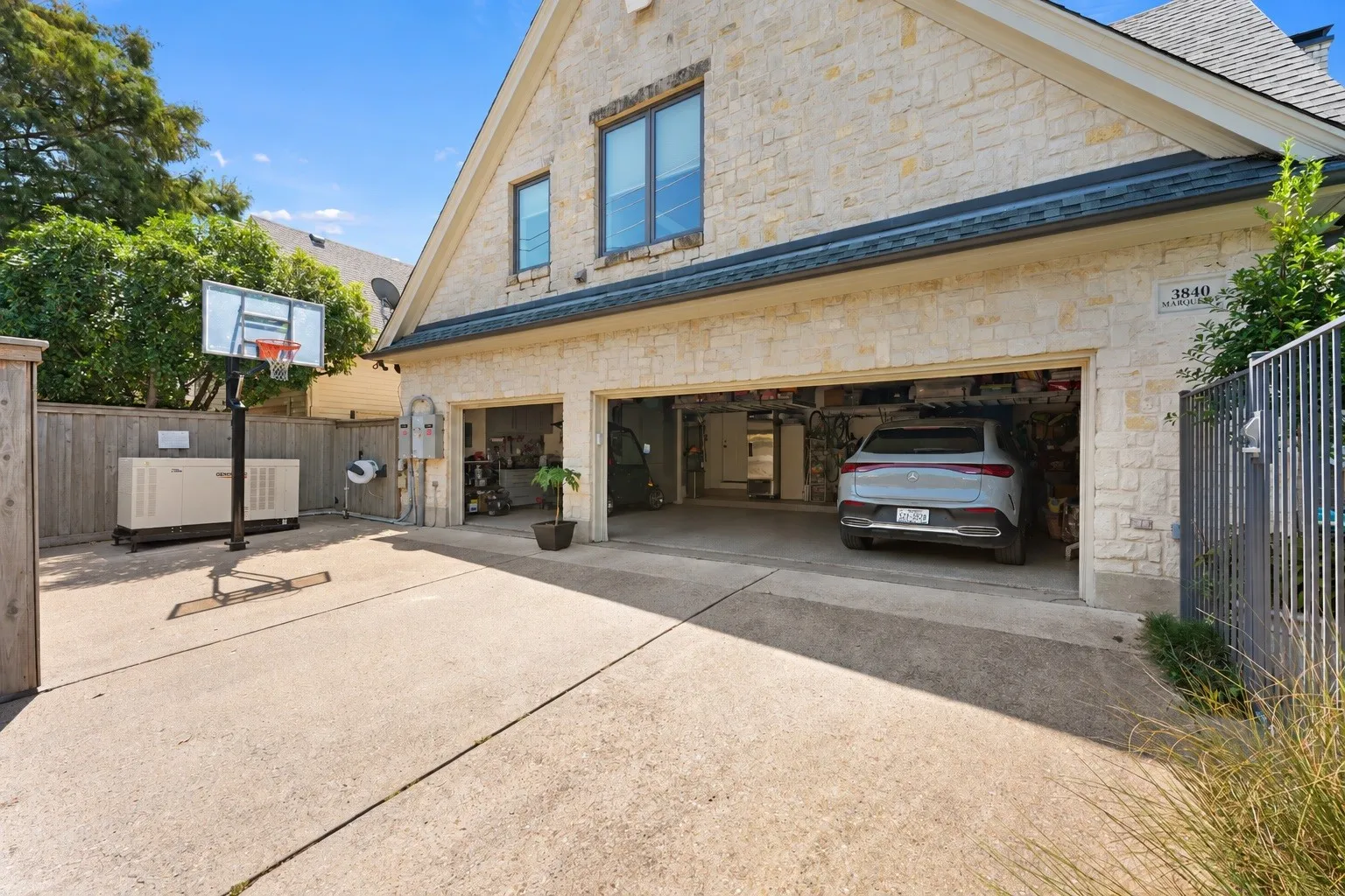 A stone-clad three-car garage with electric rear gated entry and generator positioned along the wood fence.